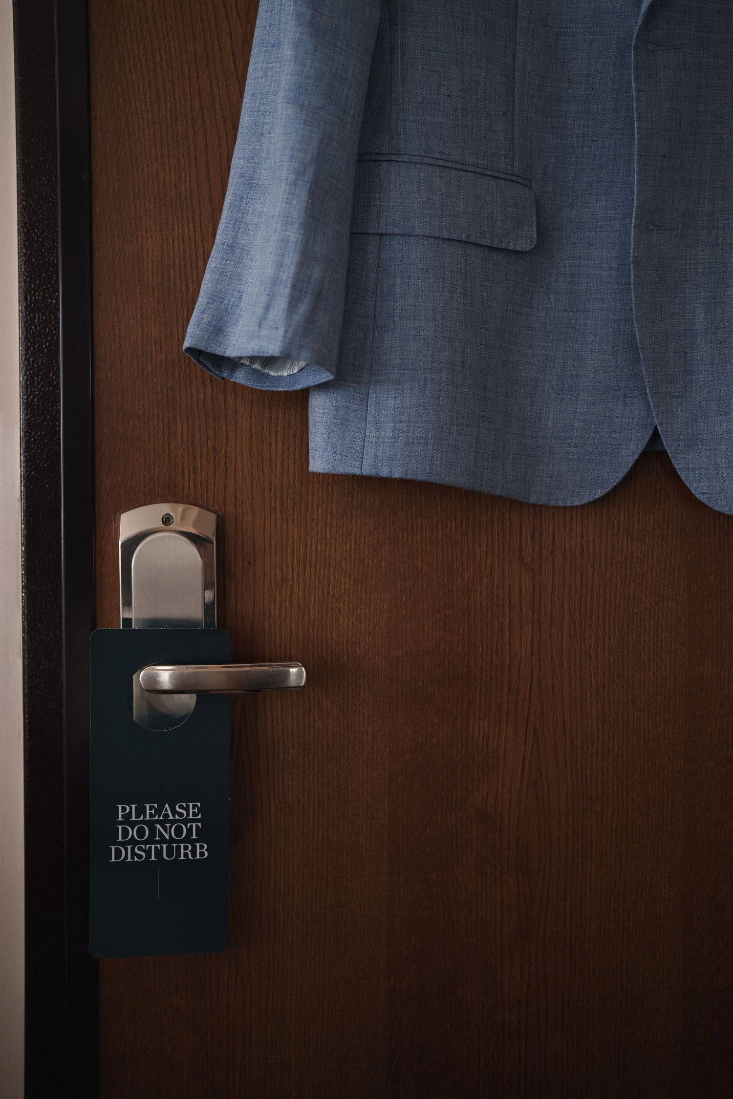 A blue suit jacket hangs near a hotel door with a Do Not Disturb sign.