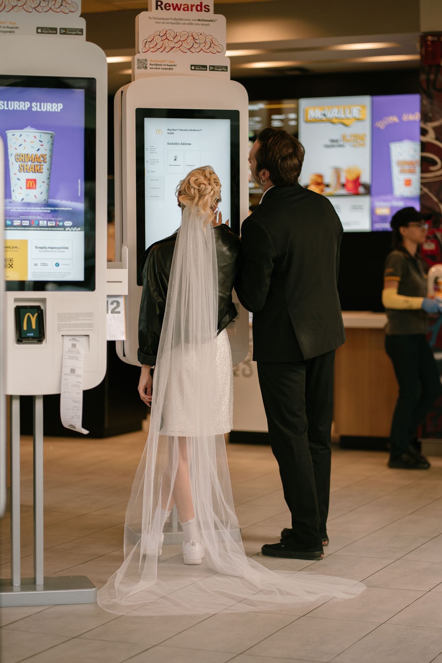 A couple in formal wear ordering McDonald from a digital kiosk at a fast food restaurant after their wedding
