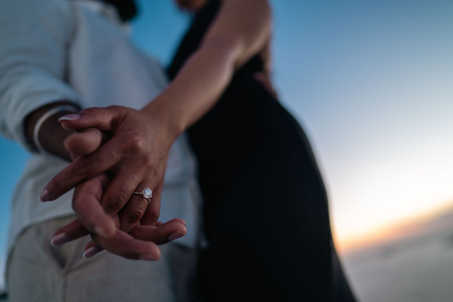 Close-up of couple holding hands against sunset backdrop with a wedding ring