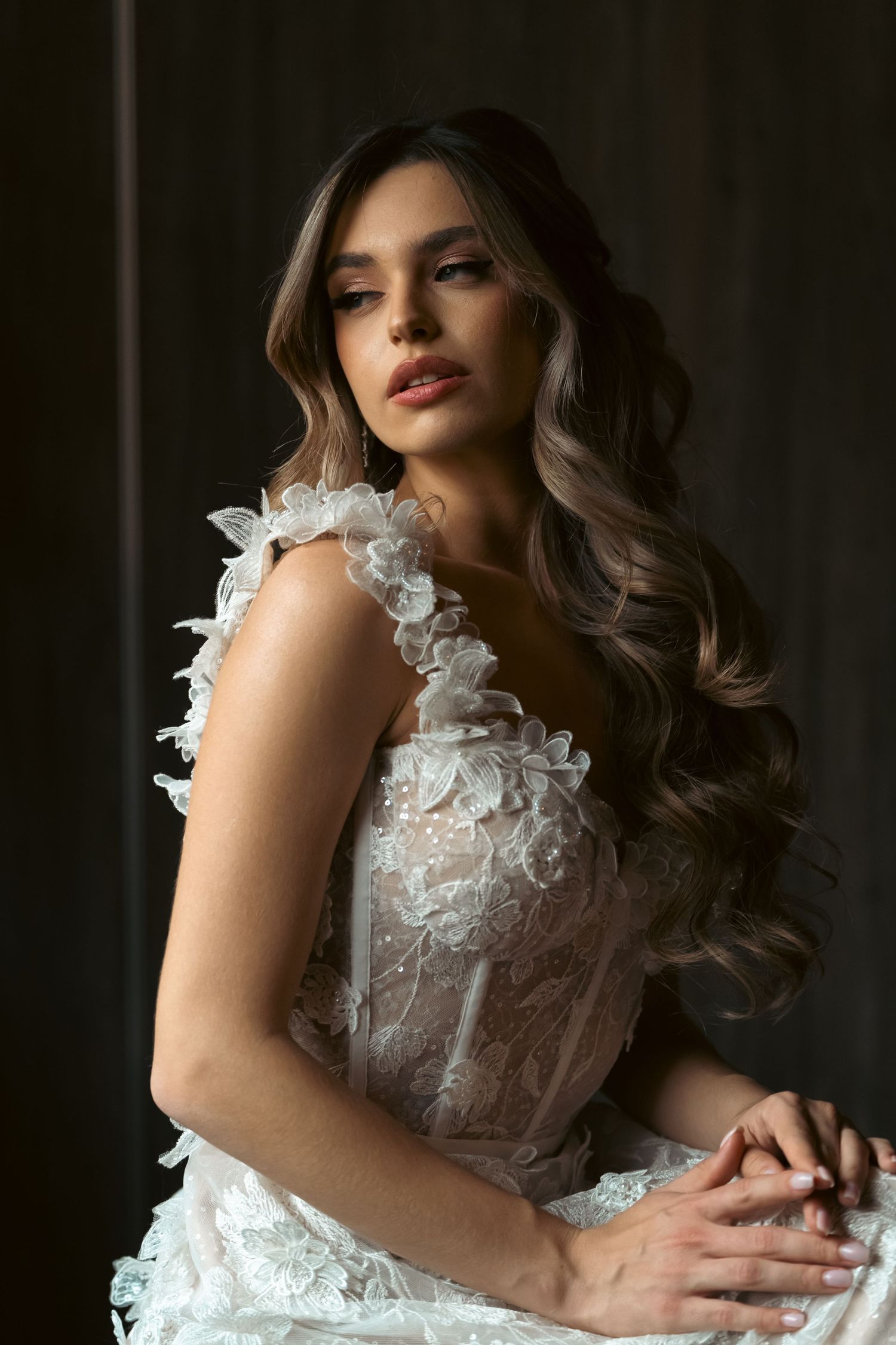 Elegant lace wedding gown with delicate floral appliques photographed against dark background.