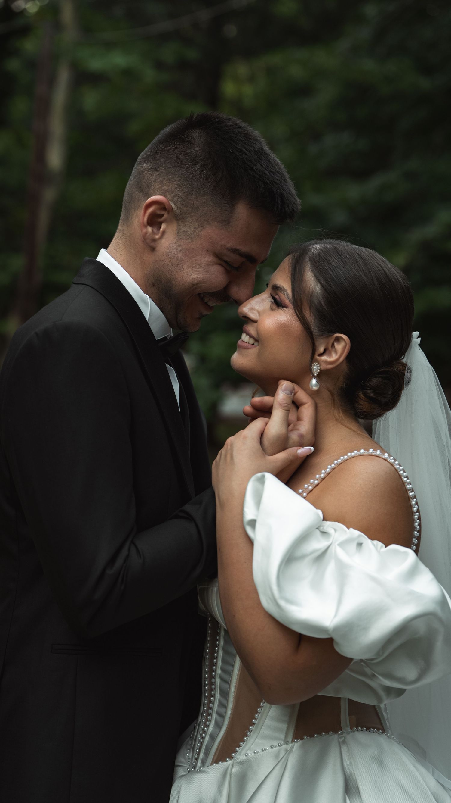 Romantic wedding couple embracing in a forest setting with the bride wearing a white gown.
