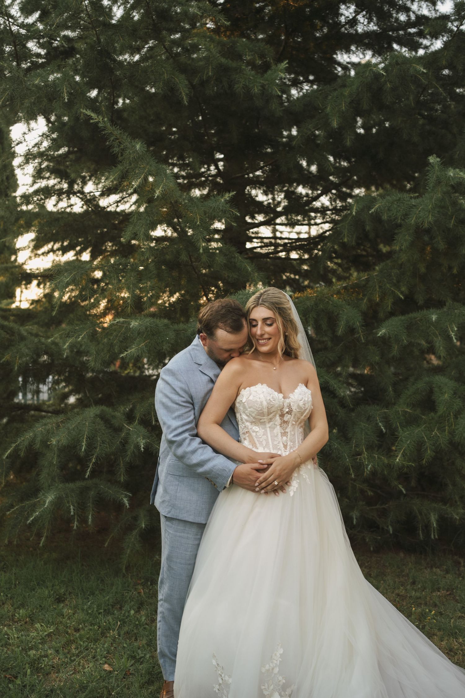 Intimate wedding couple poses in front of evergreen trees during golden hour.