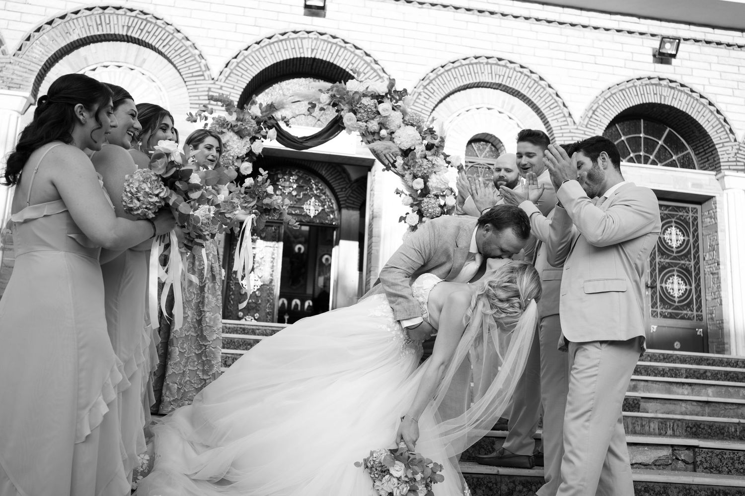 Wedding party celebrates with bubbles and laughter outside a historic building during a joyful summer ceremony.