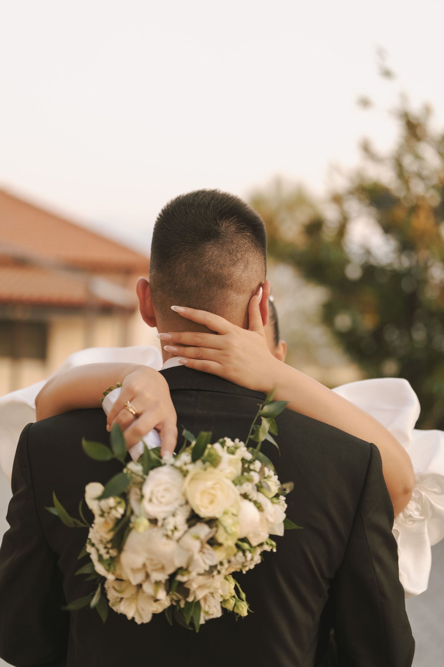 A romantic wedding moment with a white bouquet of roses and delicate embrace from behind.
