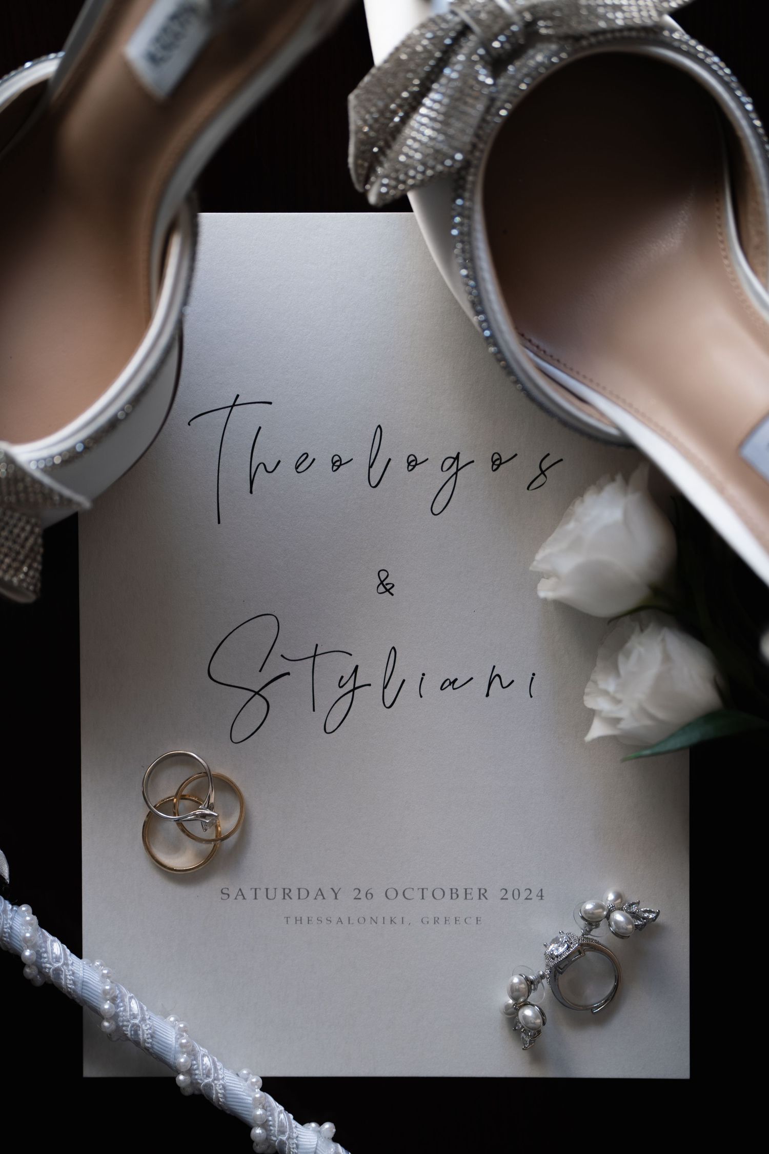 Wedding rings and jewelry photographed with elegant invitation card in soft lighting.