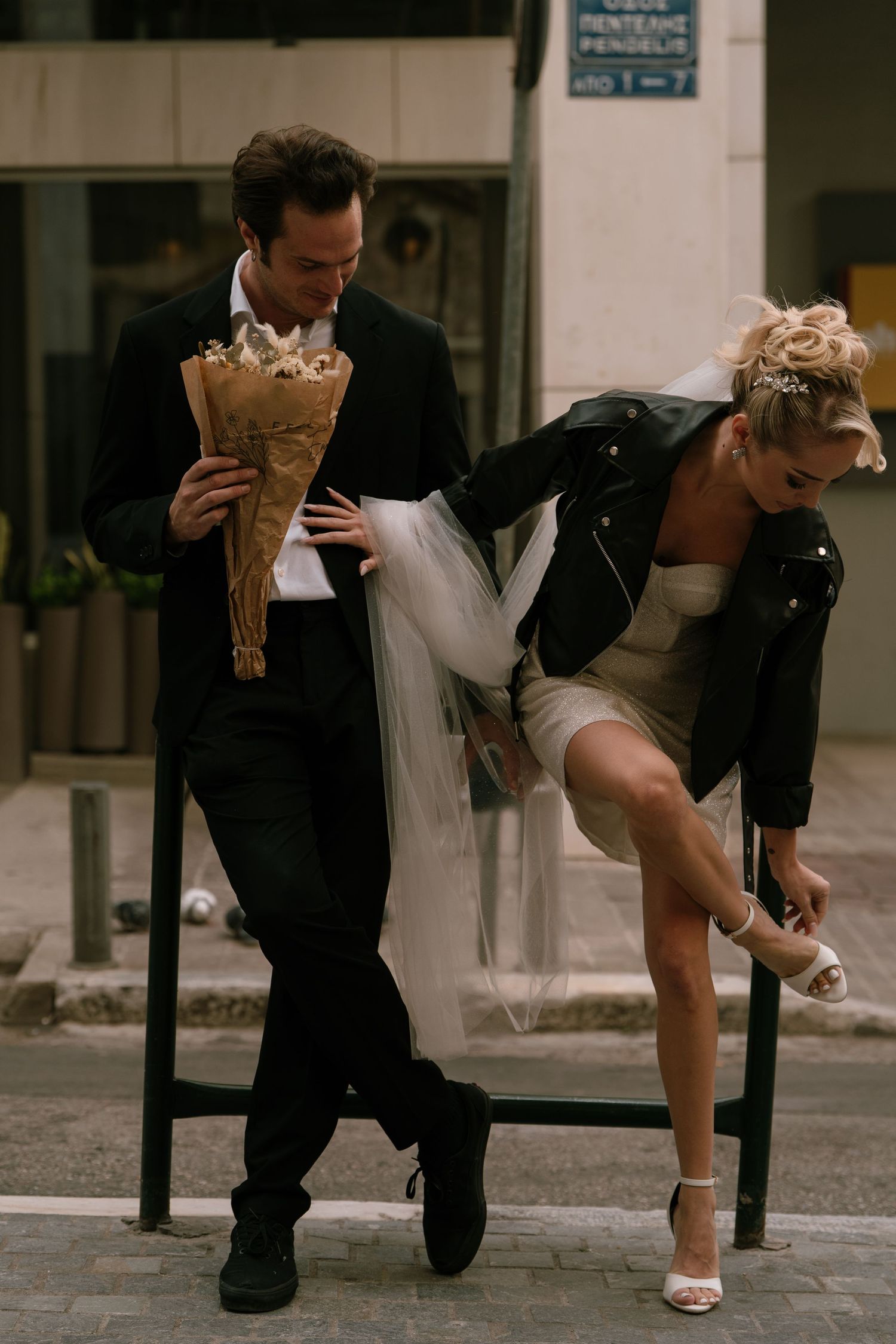 A couple in wedding attire poses playfully on a city street in Athens Greece  with a bouquet.