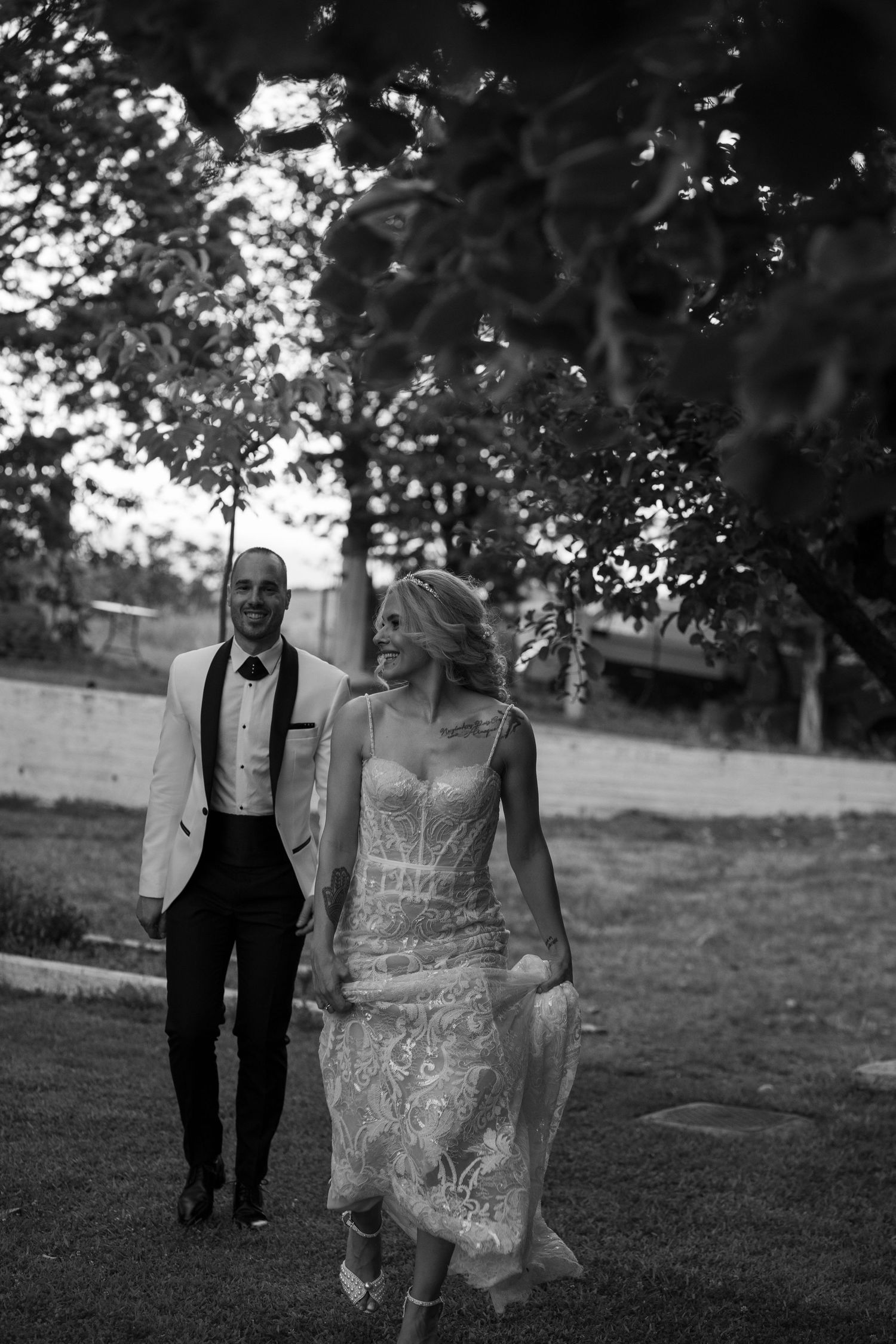 Couple walking through a scenic outdoor garden setting in formal attire.