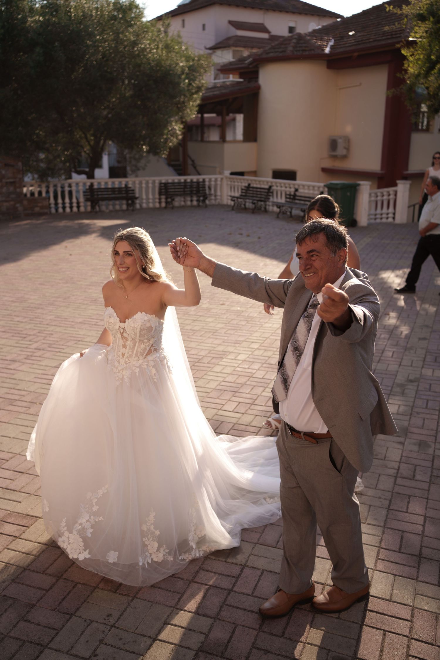 A couple in wedding attire performs a romantic dance sequence on a stone patio outside a Mediterranean-style building.