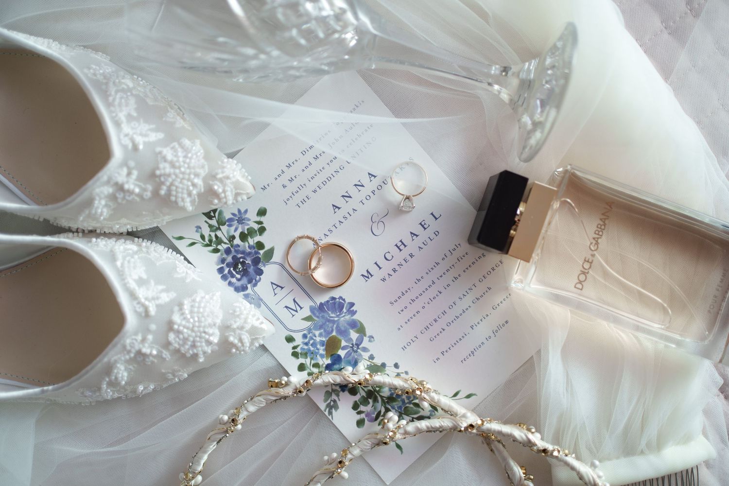 Wedding details including rings and invitations arranged on white fabric.