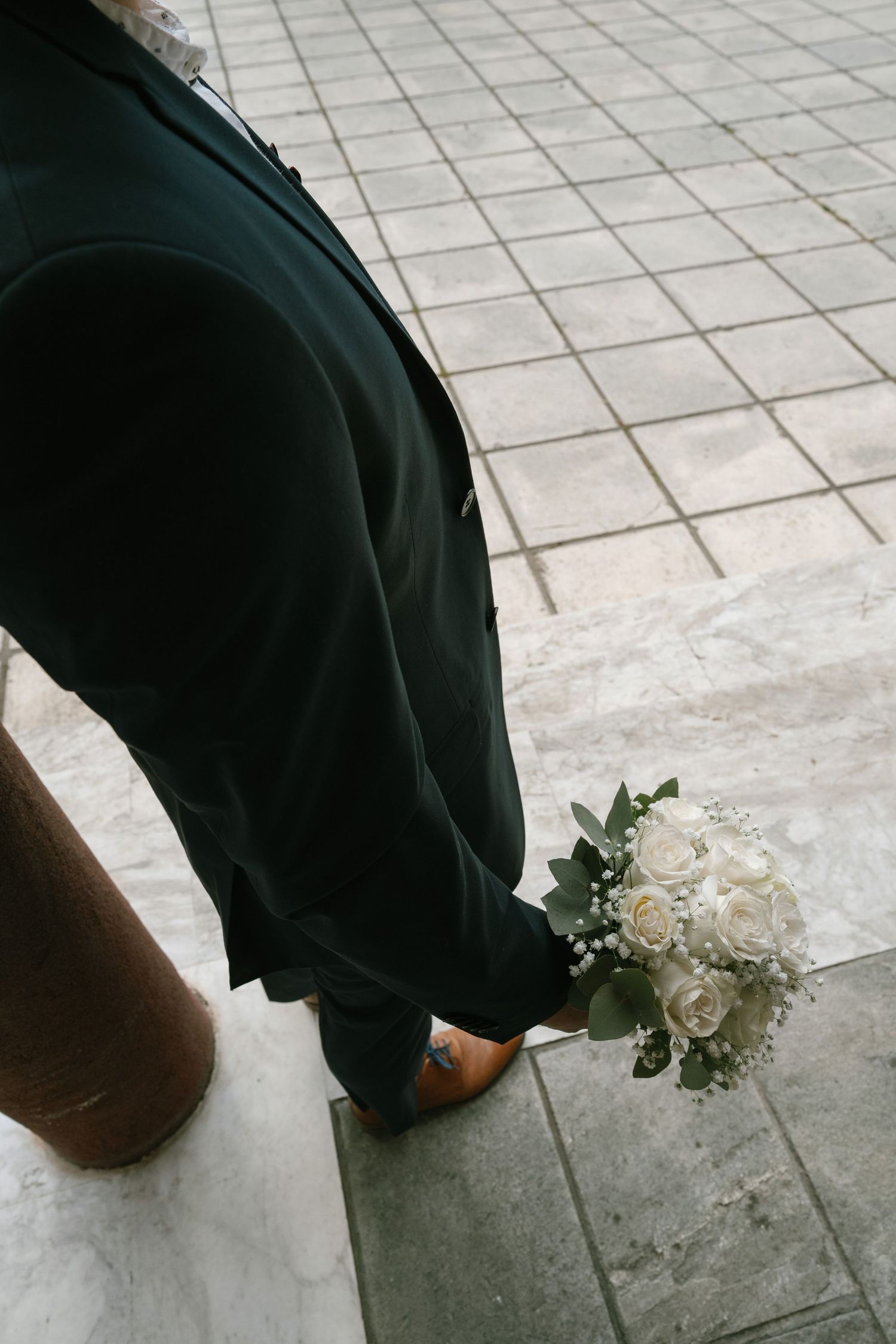 White wedding bouquet resting on grey stone tiles with black fabric in frame.