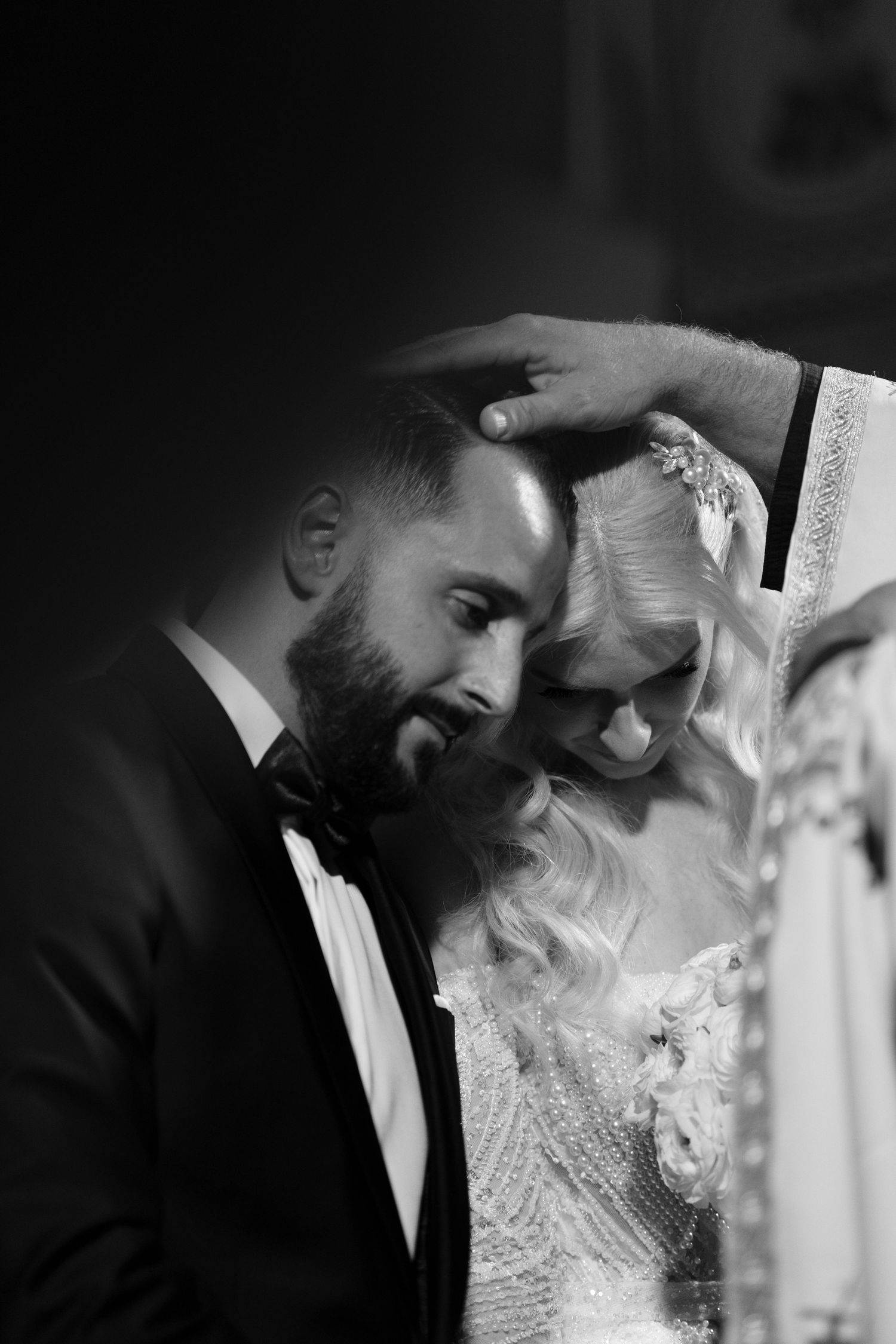 Intimate black and white wedding portrait with dramatic lighting and formal attire.
