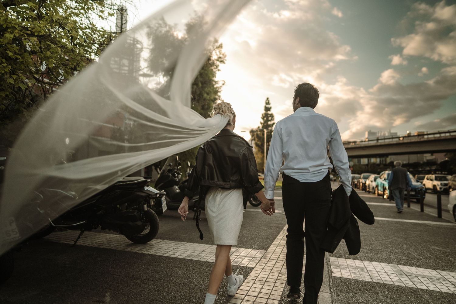 A wedding couple walks down a street at sunset with a flowing veil catching the golden light in Athens Greece