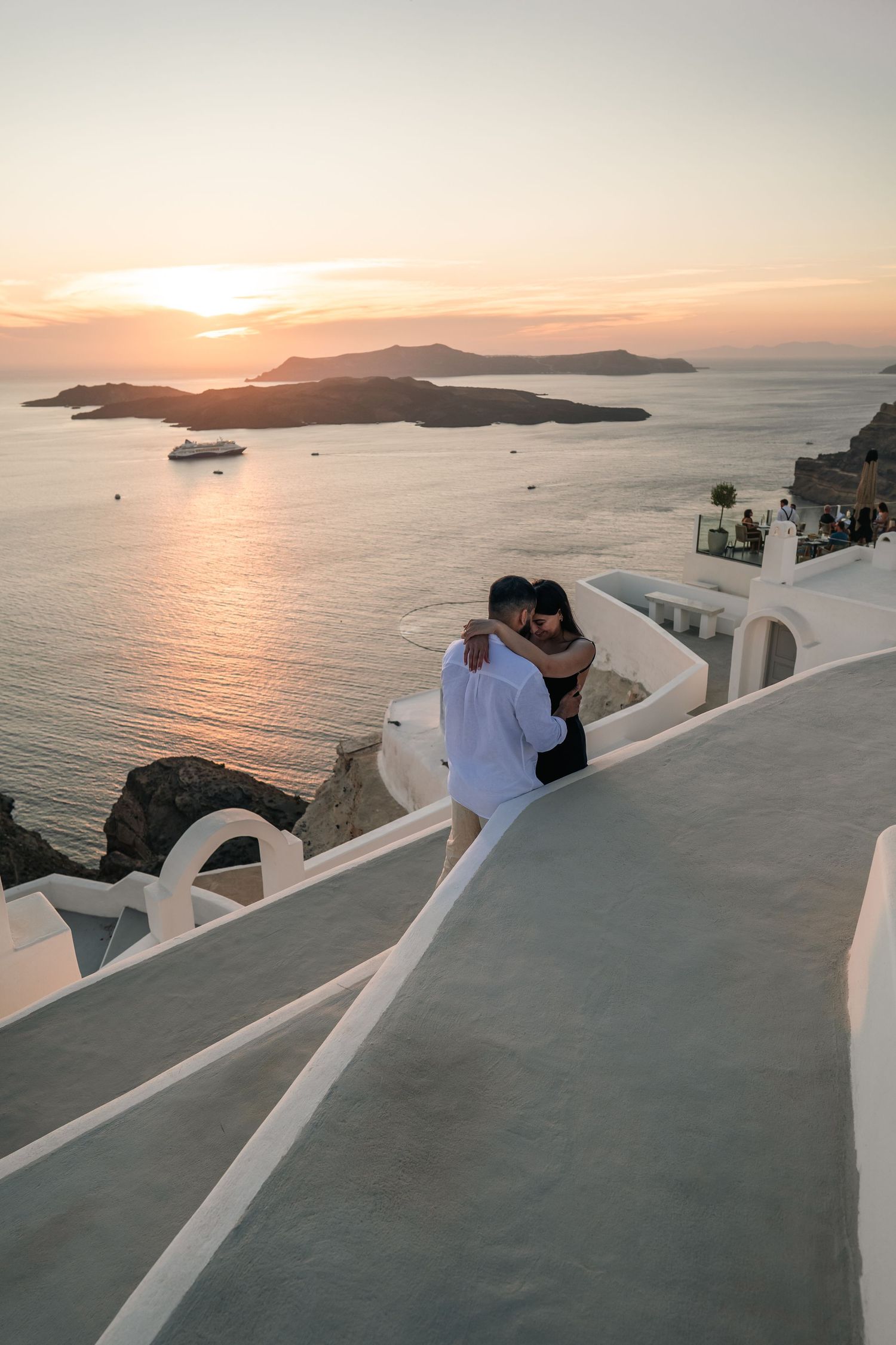 Romantic couple watching sunset over Mediterranean islands from white Santorini balcony.