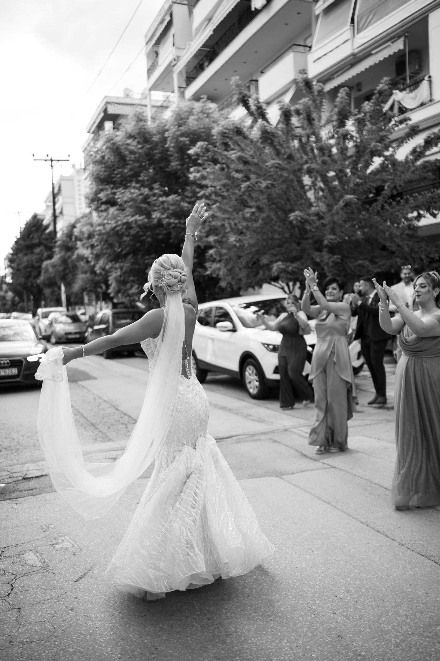 Bride in flowing white dress twirling on city street with wedding party looking on.
