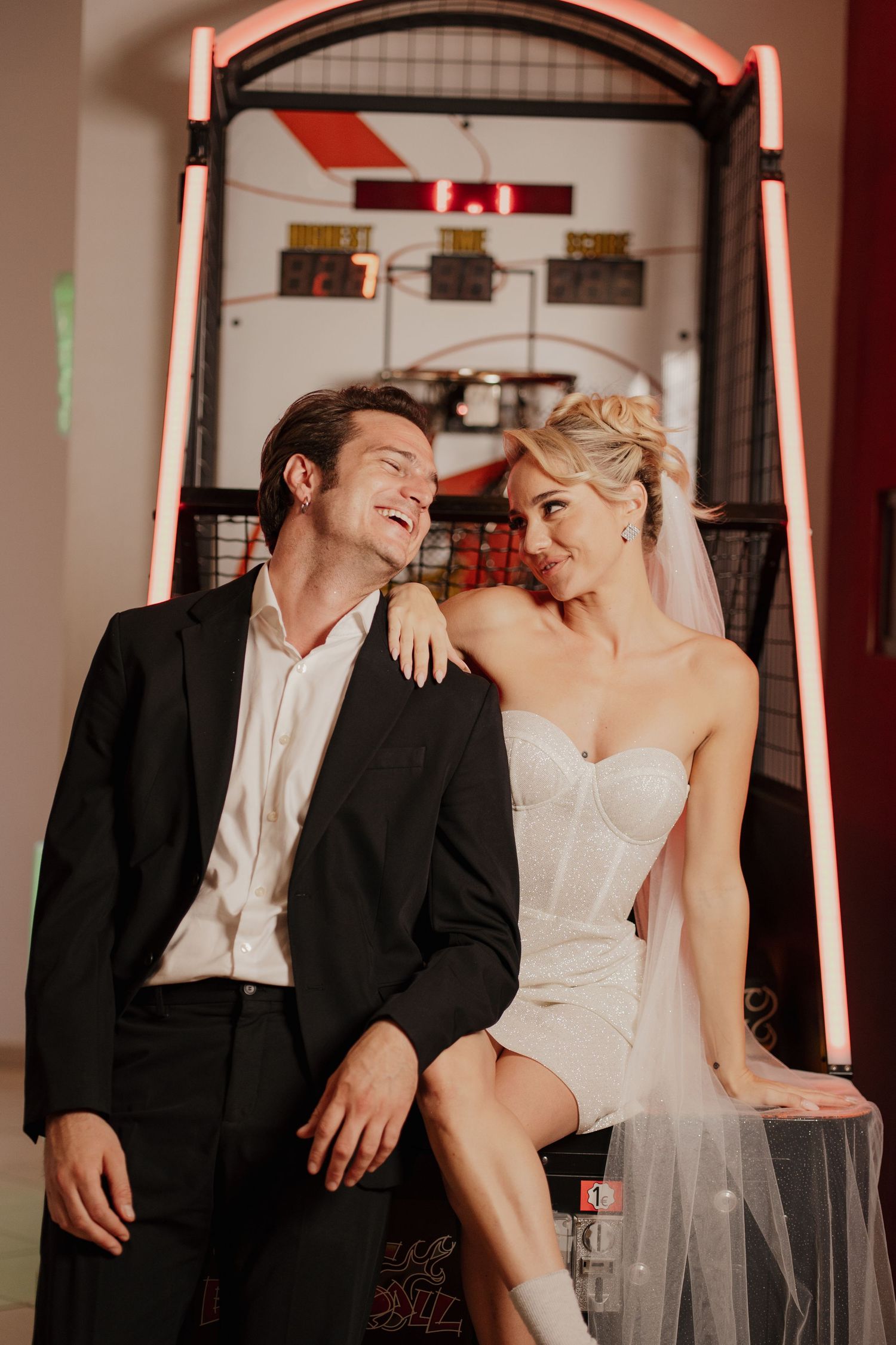 A romantic couple sharing a laugh together in front of an arcade game while the getaway from their wedding