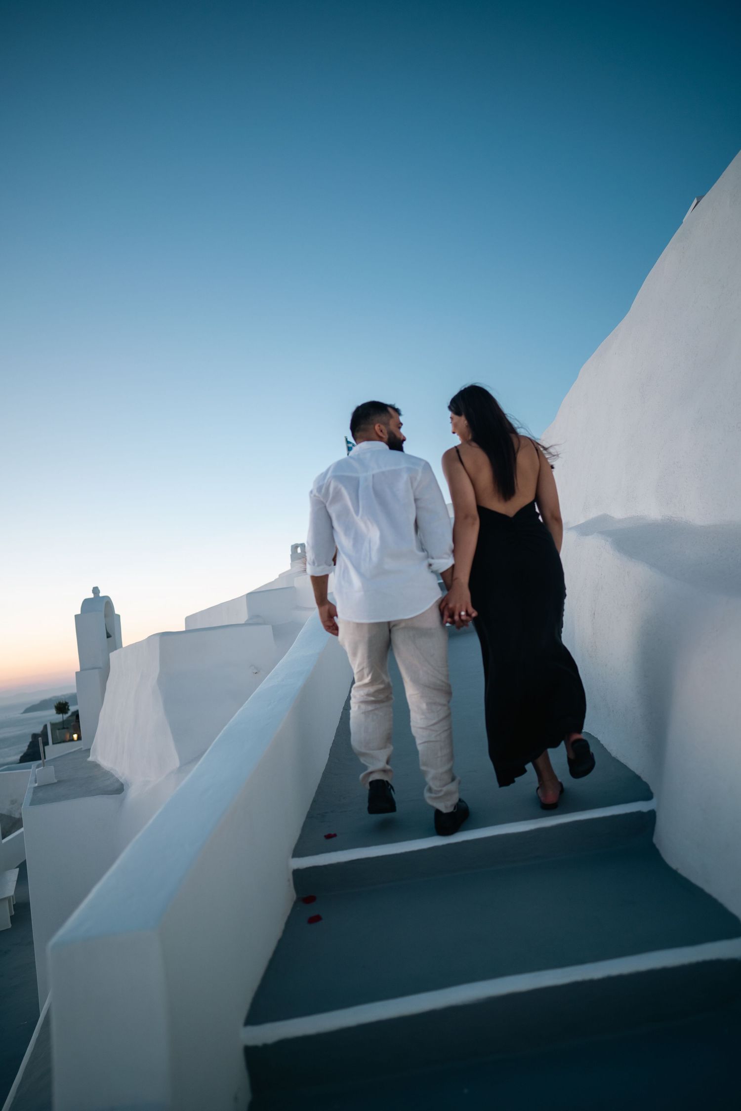 Couple walking up white curved steps in Santorini at dusk.