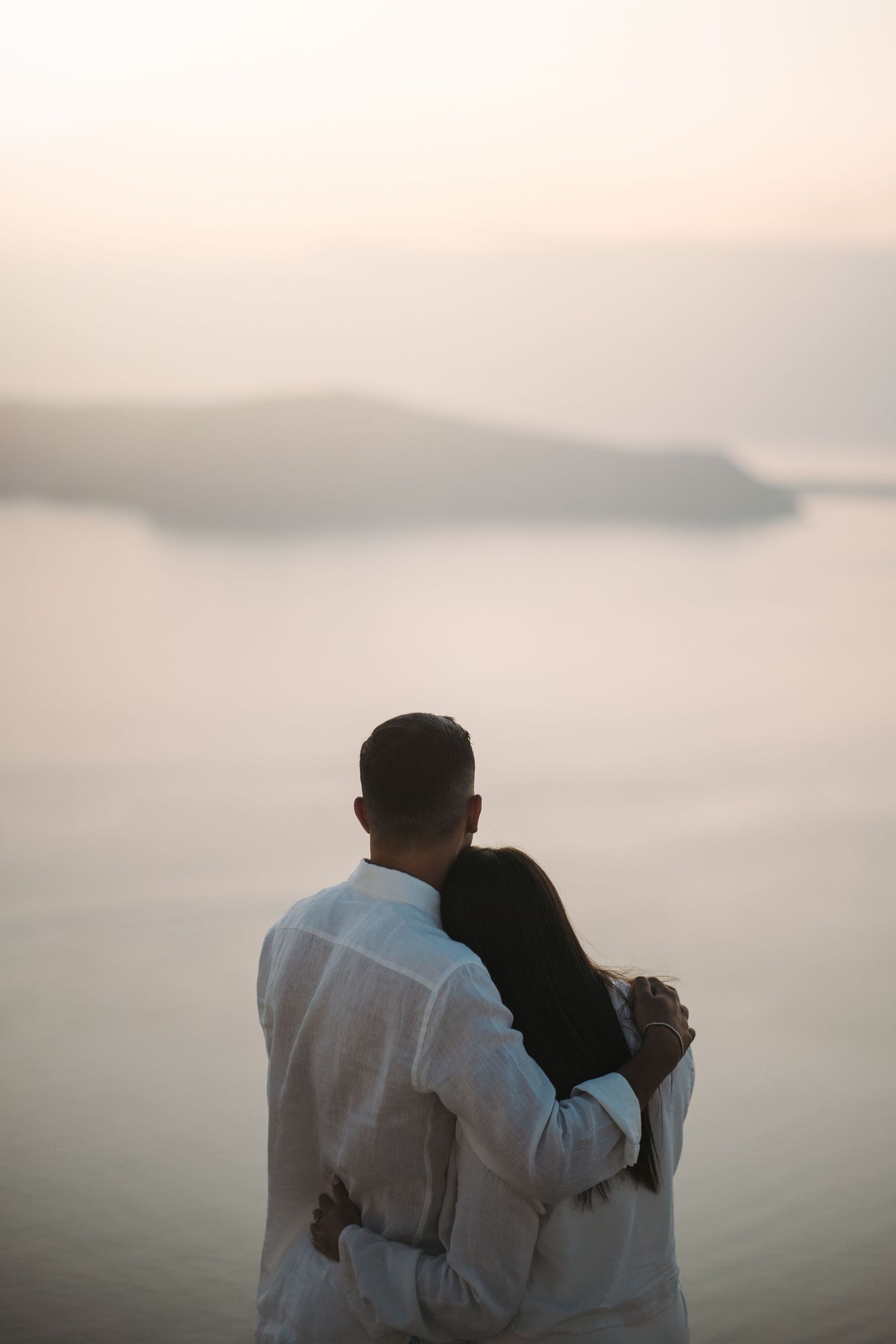 Silhouetted couple embracing against a misty mountain landscape at sunset.