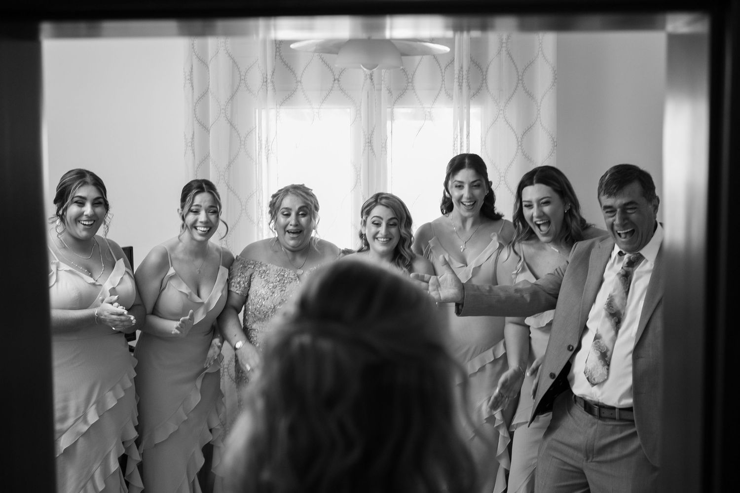 Black and white photo of wedding party gathered in sunlit room.