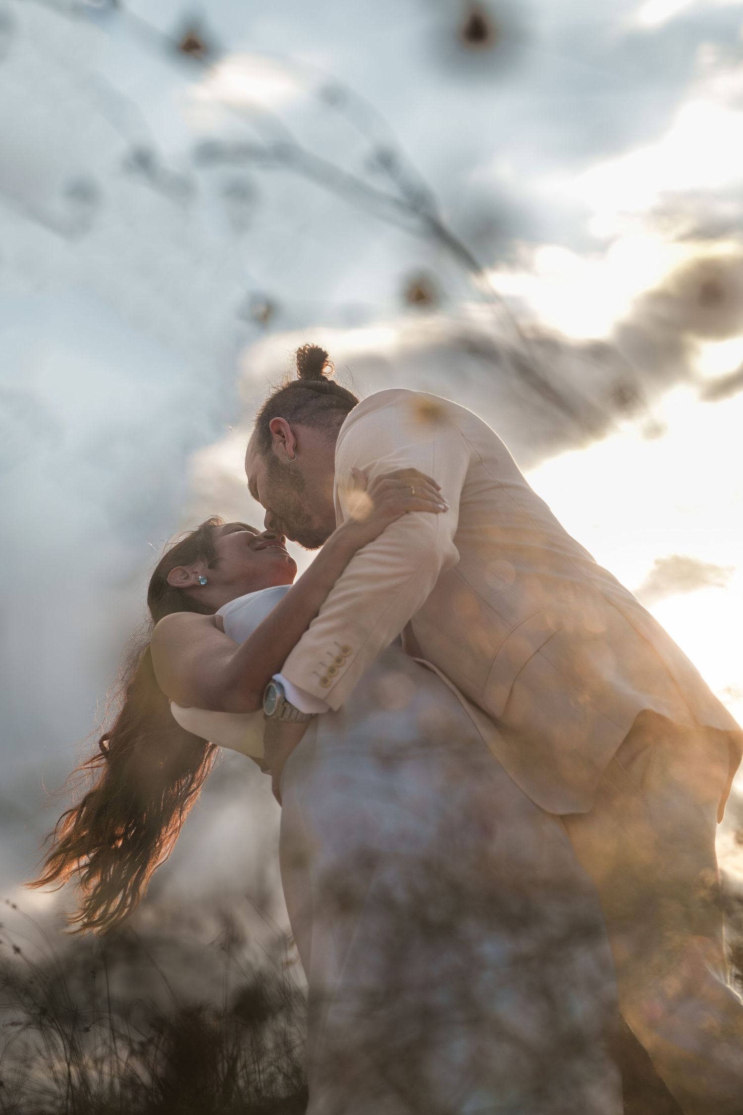 A romantic couple embraces in a dramatic backlit sunset scene with flowing hair and ethereal lighting.