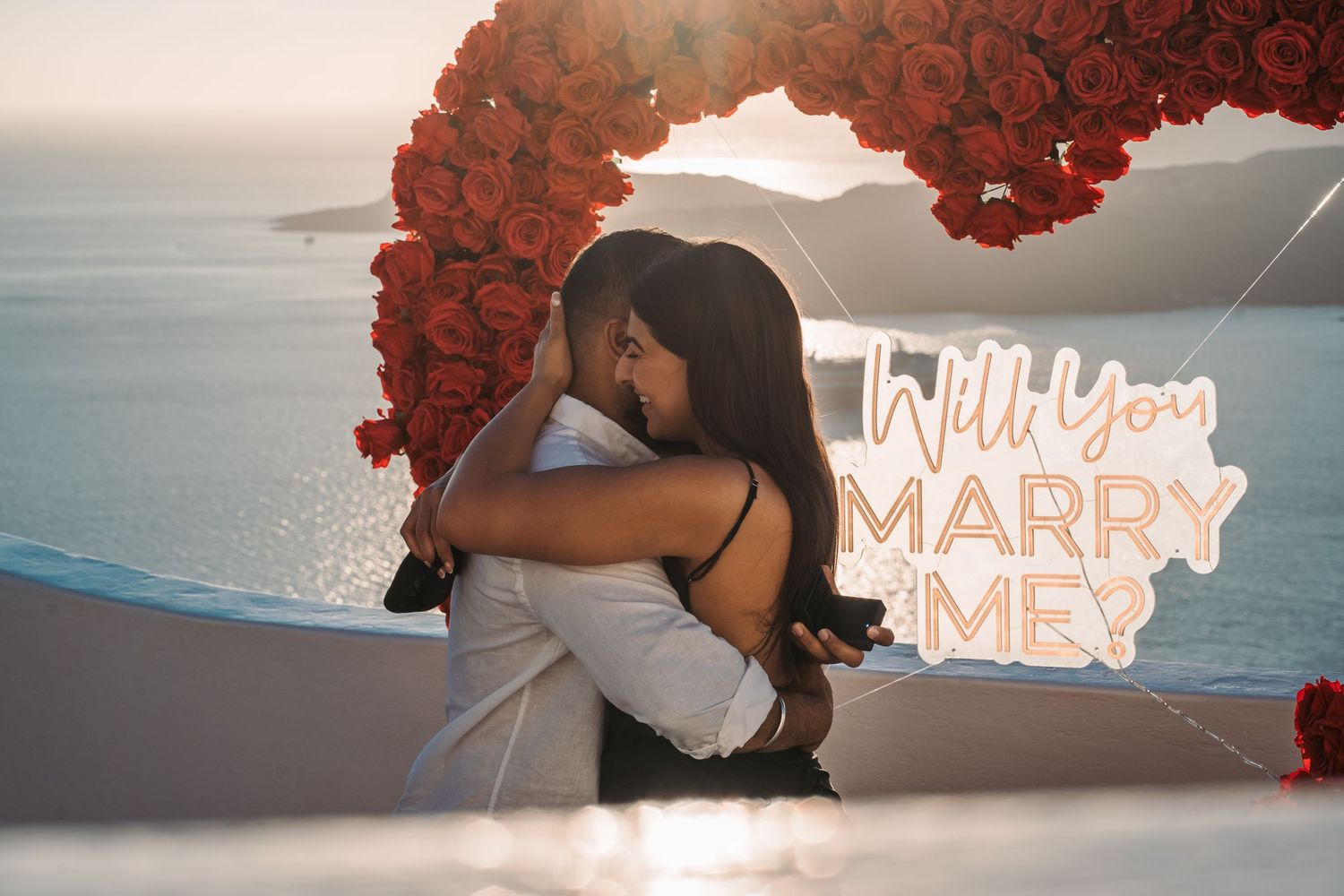 Marriage proposal setup with red heart arch and illuminated letters at oceanside in santorini