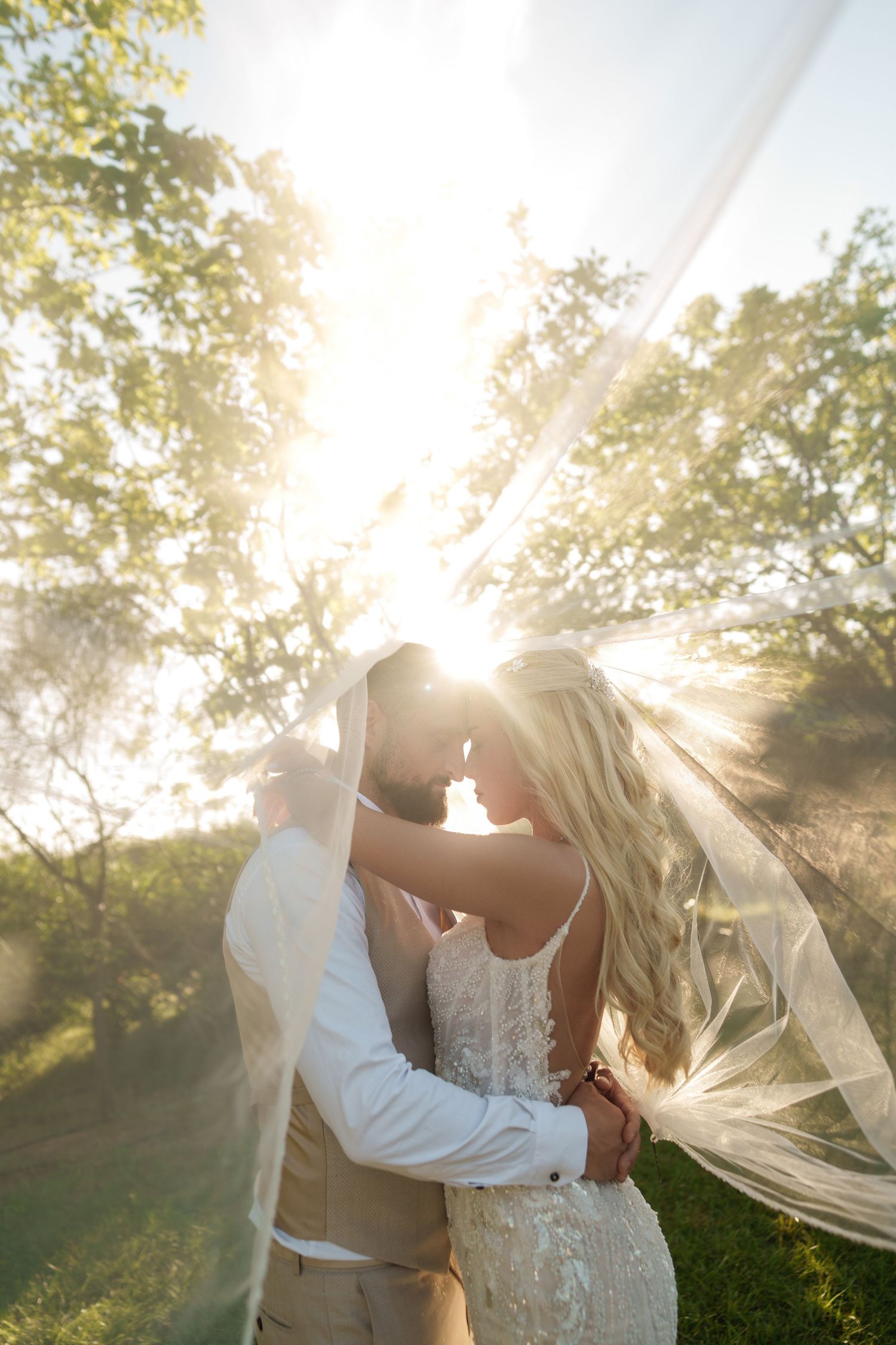 Newlyweds sharing an intimate moment in golden sunlight with flowing veil.