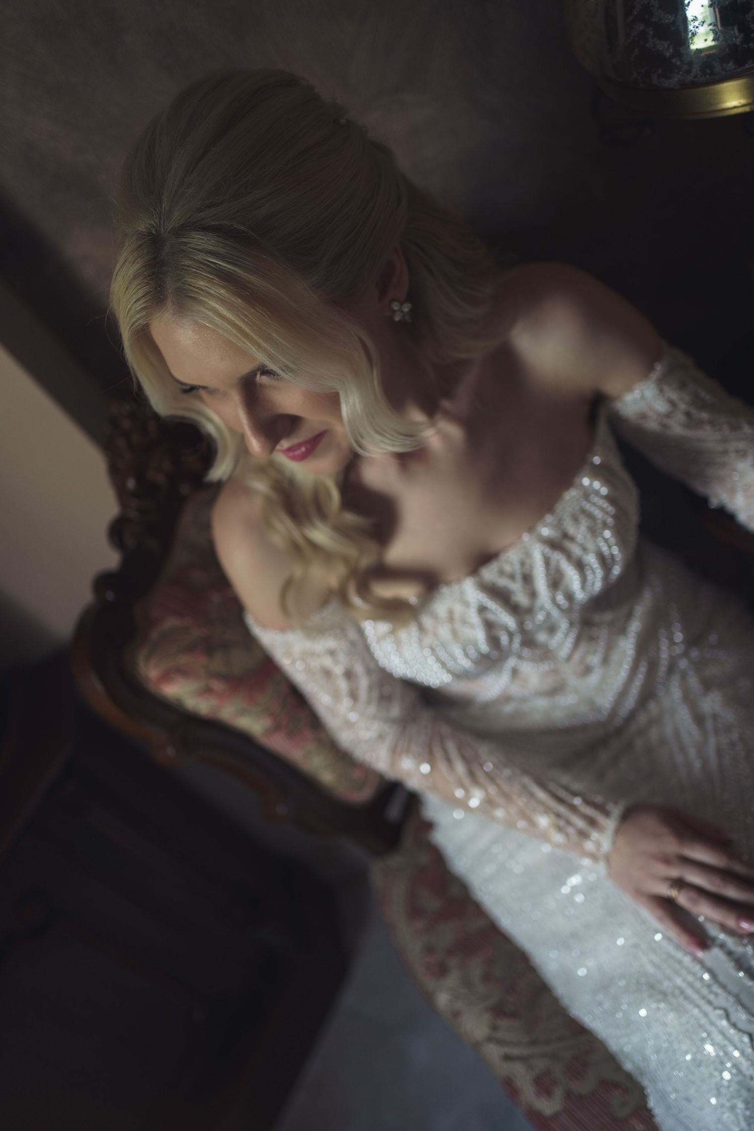 Bride in sparkling white gown poses in dramatic lighting.