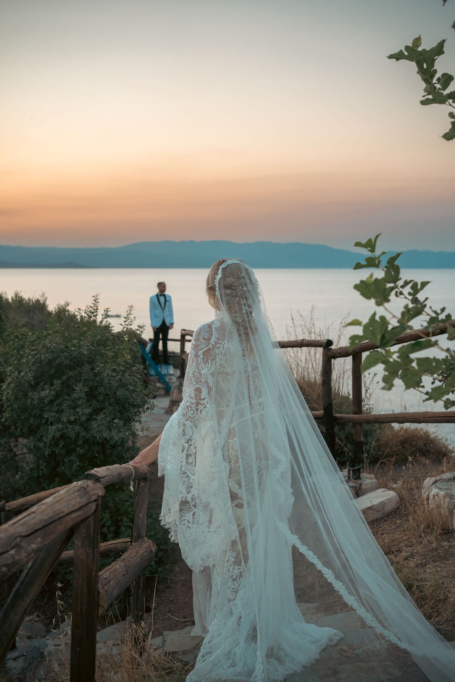 Wedding couple silhouetted against a scenic coastal sunset view with wooden railings.