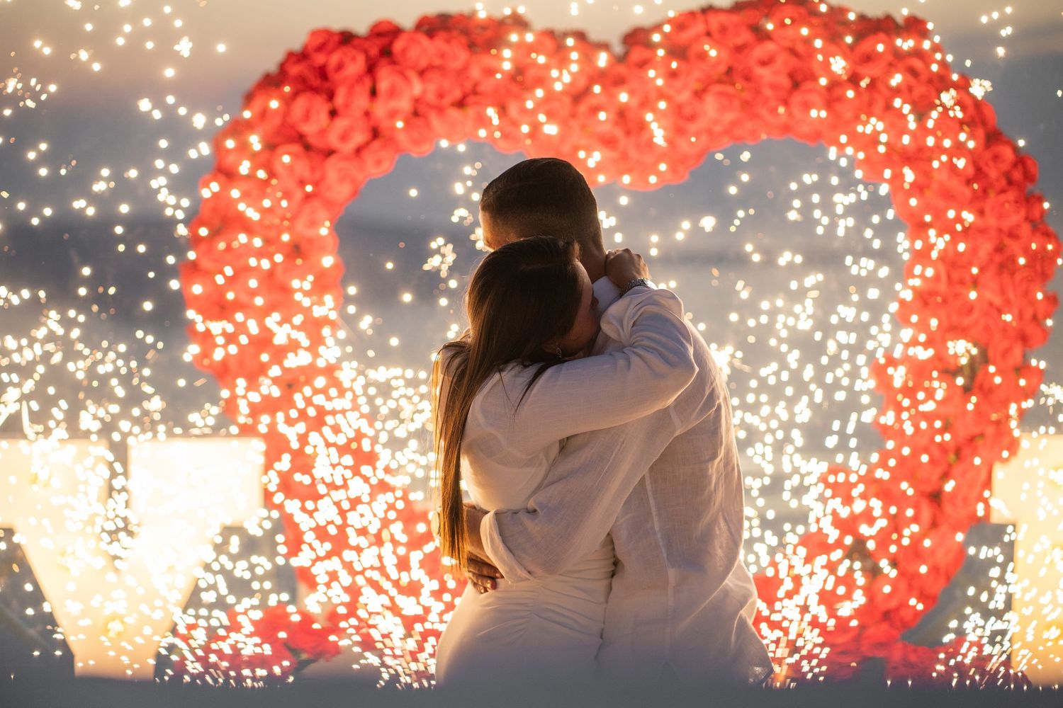 Romantic proposal moment with dramatic red fireworks display in the background.