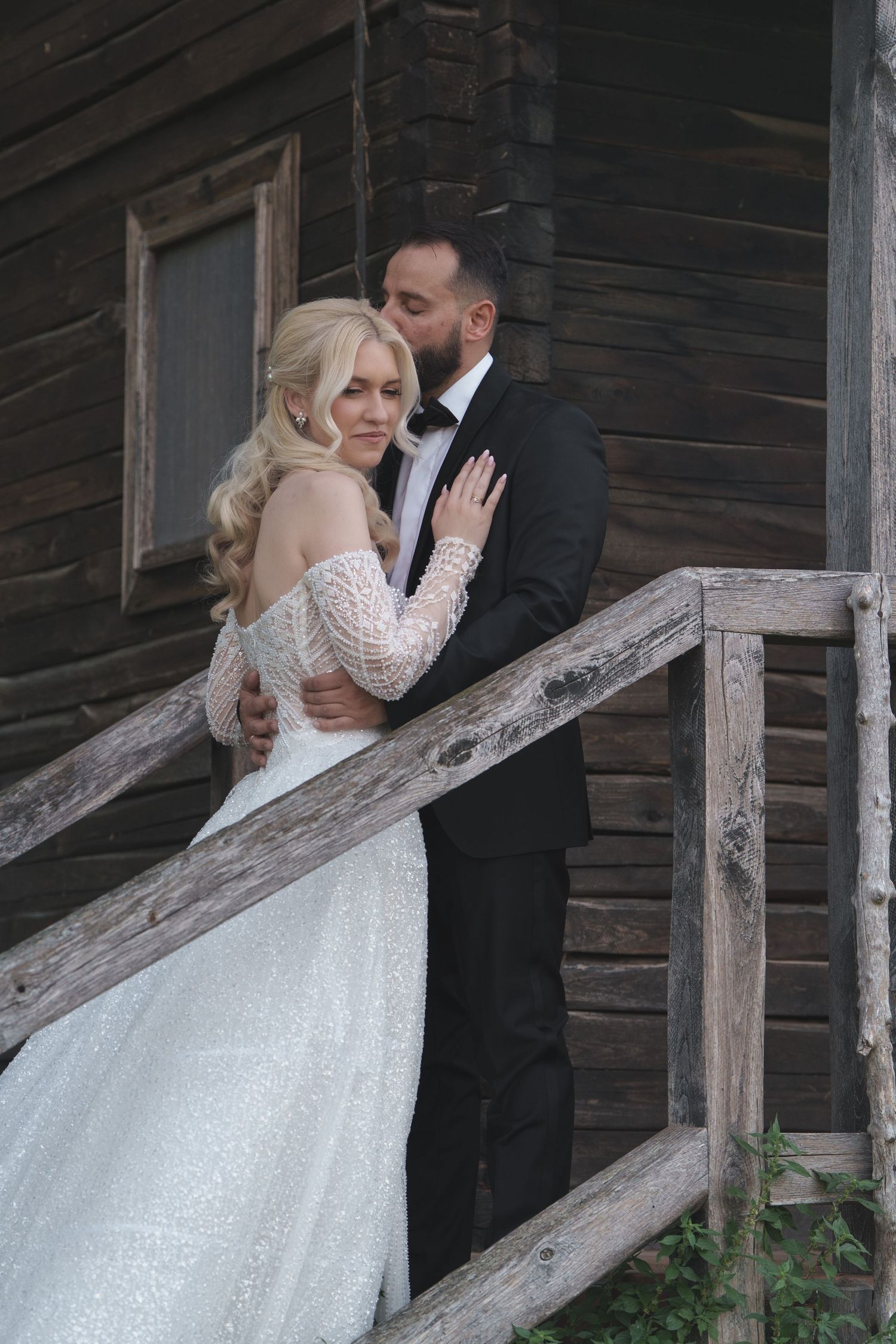 Wedding couple embracing on rustic wooden porch steps of vintage barn.