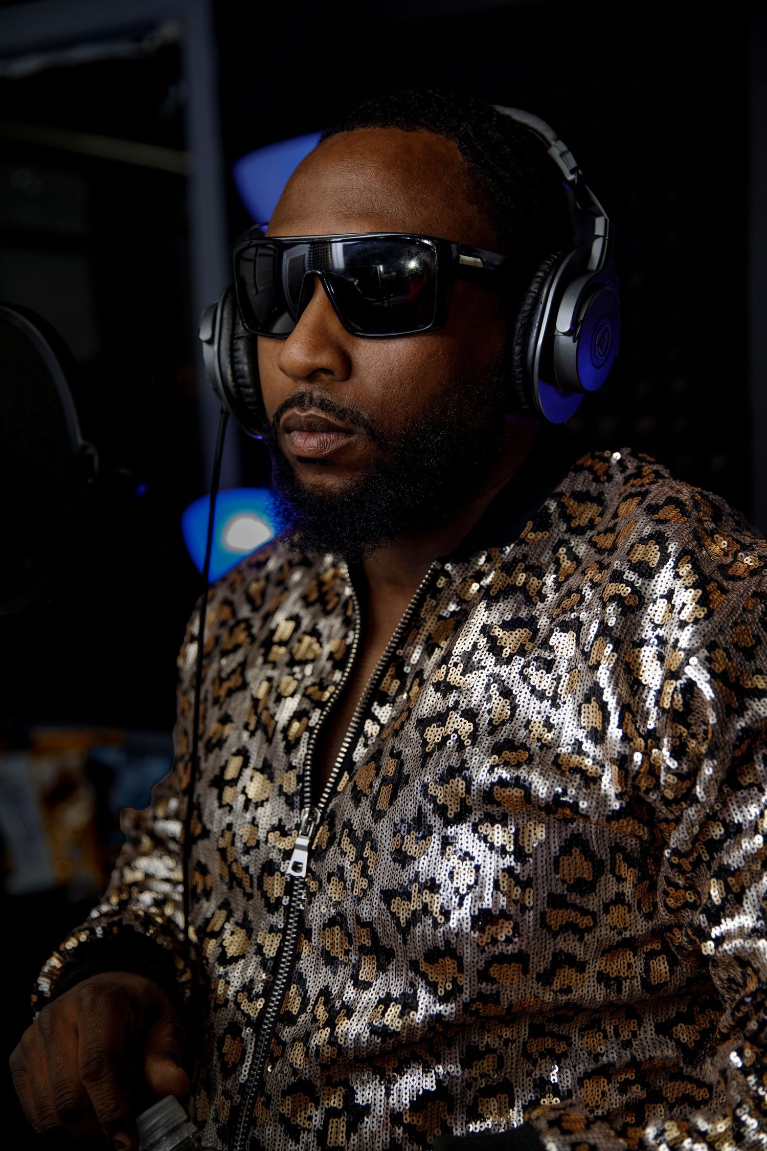 DJ wearing headphones and a sequined animal print jacket performs in dramatic lighting.