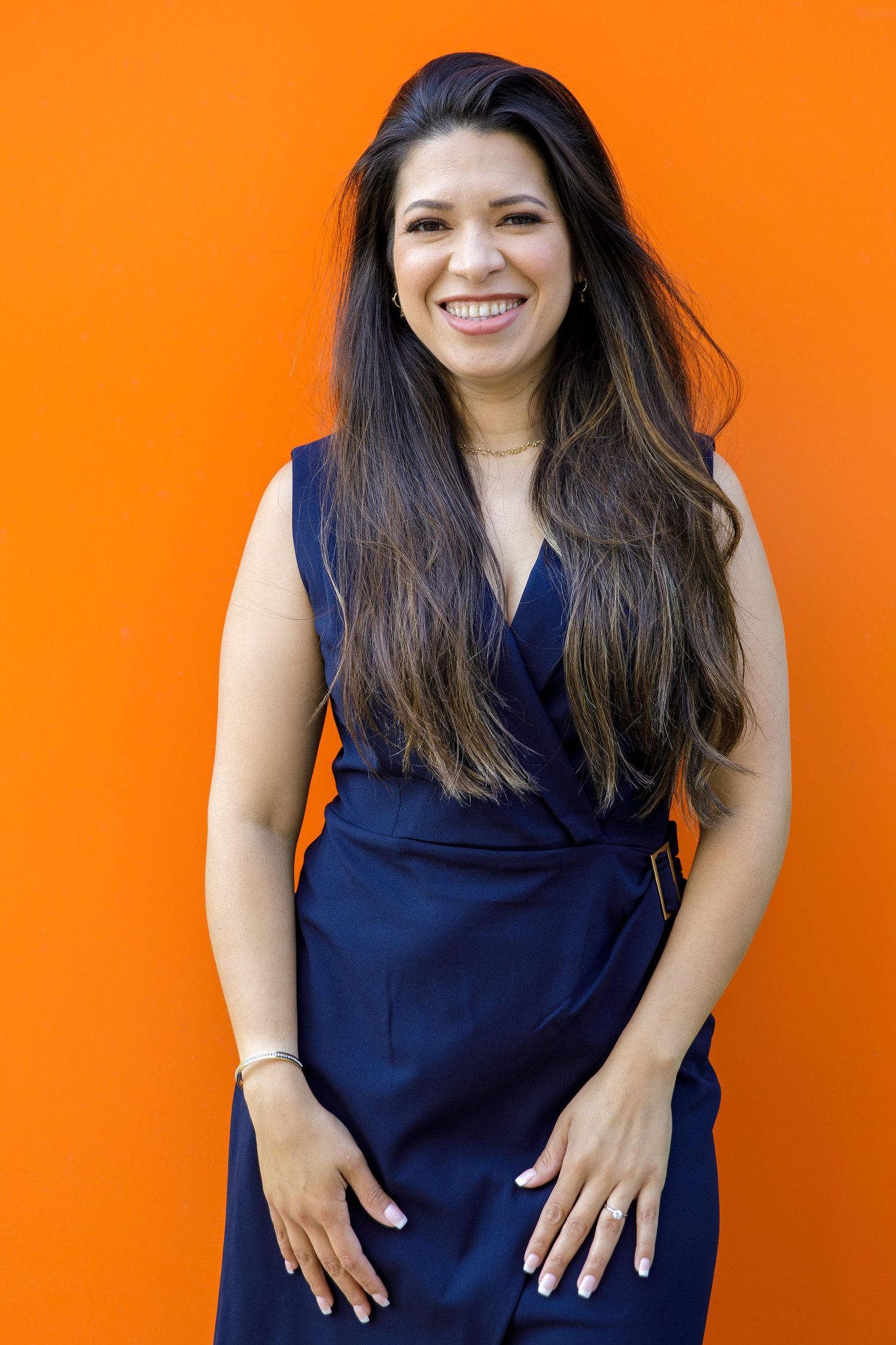 Portrait of person in navy wrap dress smiling against bright orange wall.