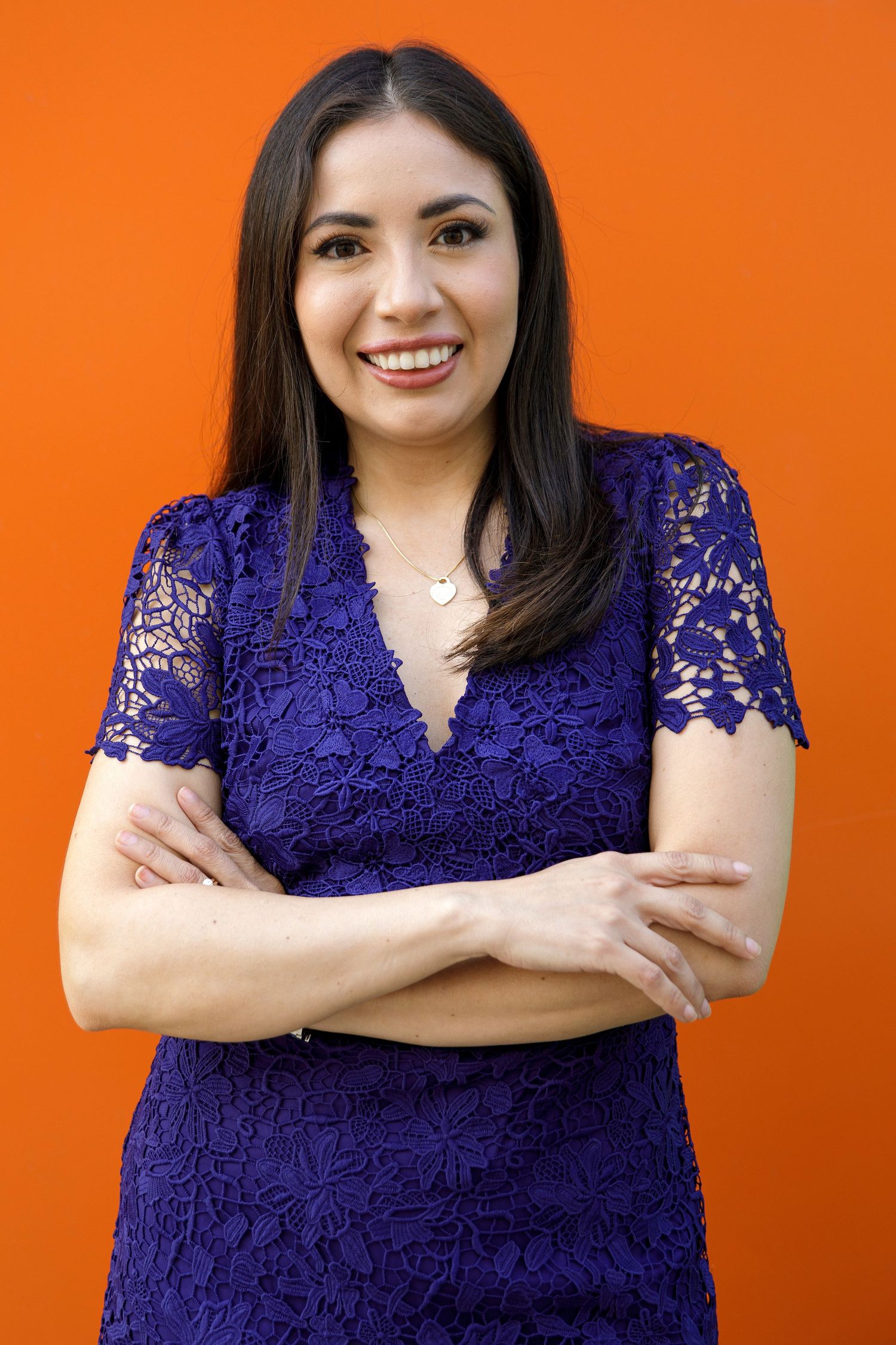 Portrait of person wearing purple lace dress against vivid orange background.