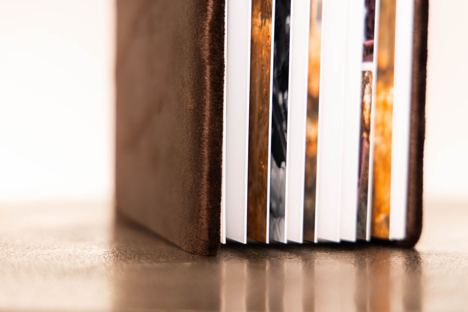 Close-up of a leather-bound photo book standing upright, showing layered pages with colorful printed photographs inside.