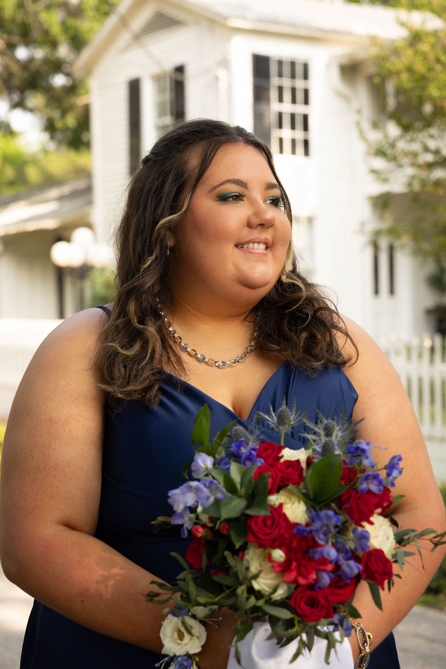 Woman in navy blue bridesmaid dress holding colorful bouquet of red, white, and blue flowers outdoors.