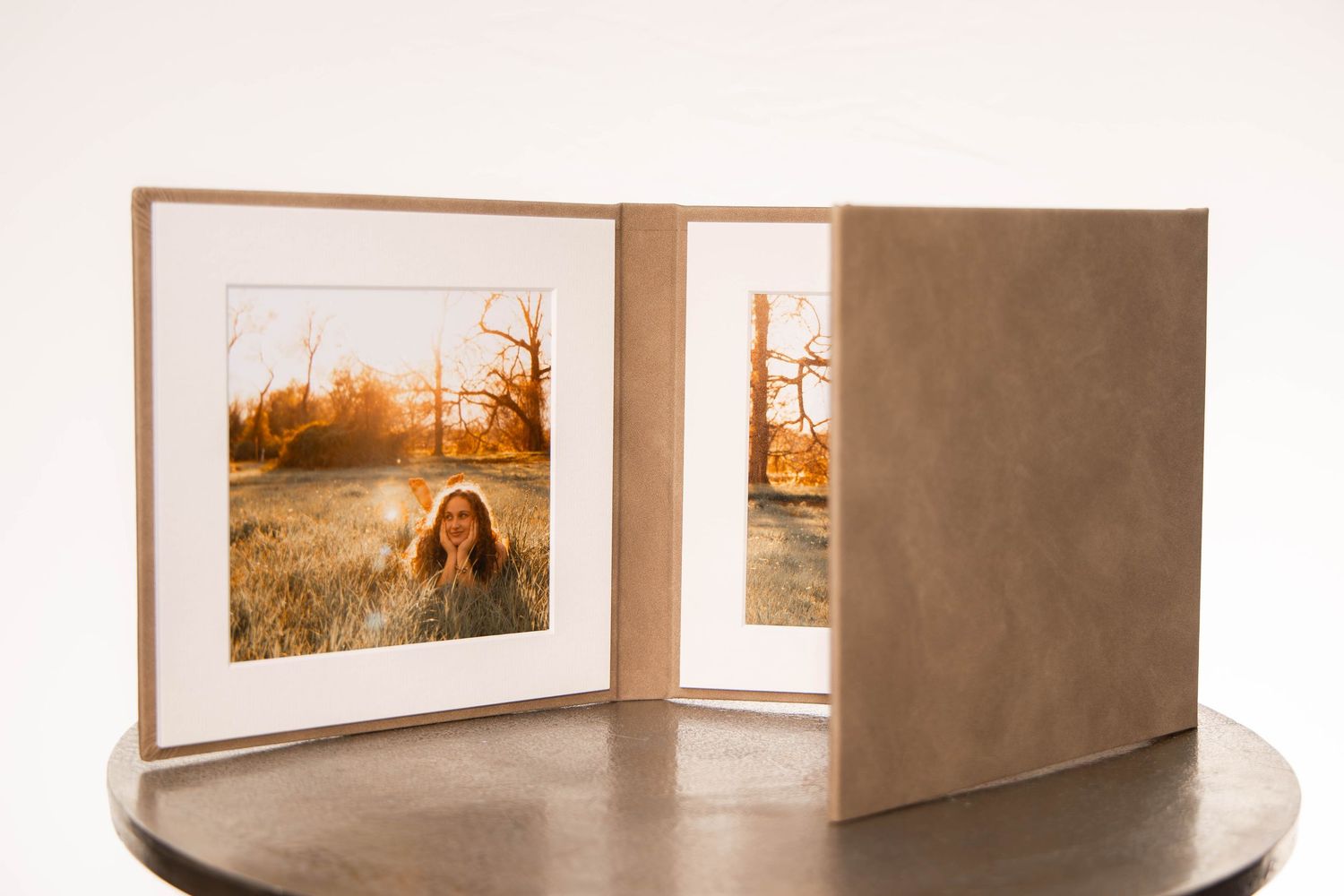 Elegant suede photo folio open displaying two warm-toned sunset portrait prints of a girl in a field.