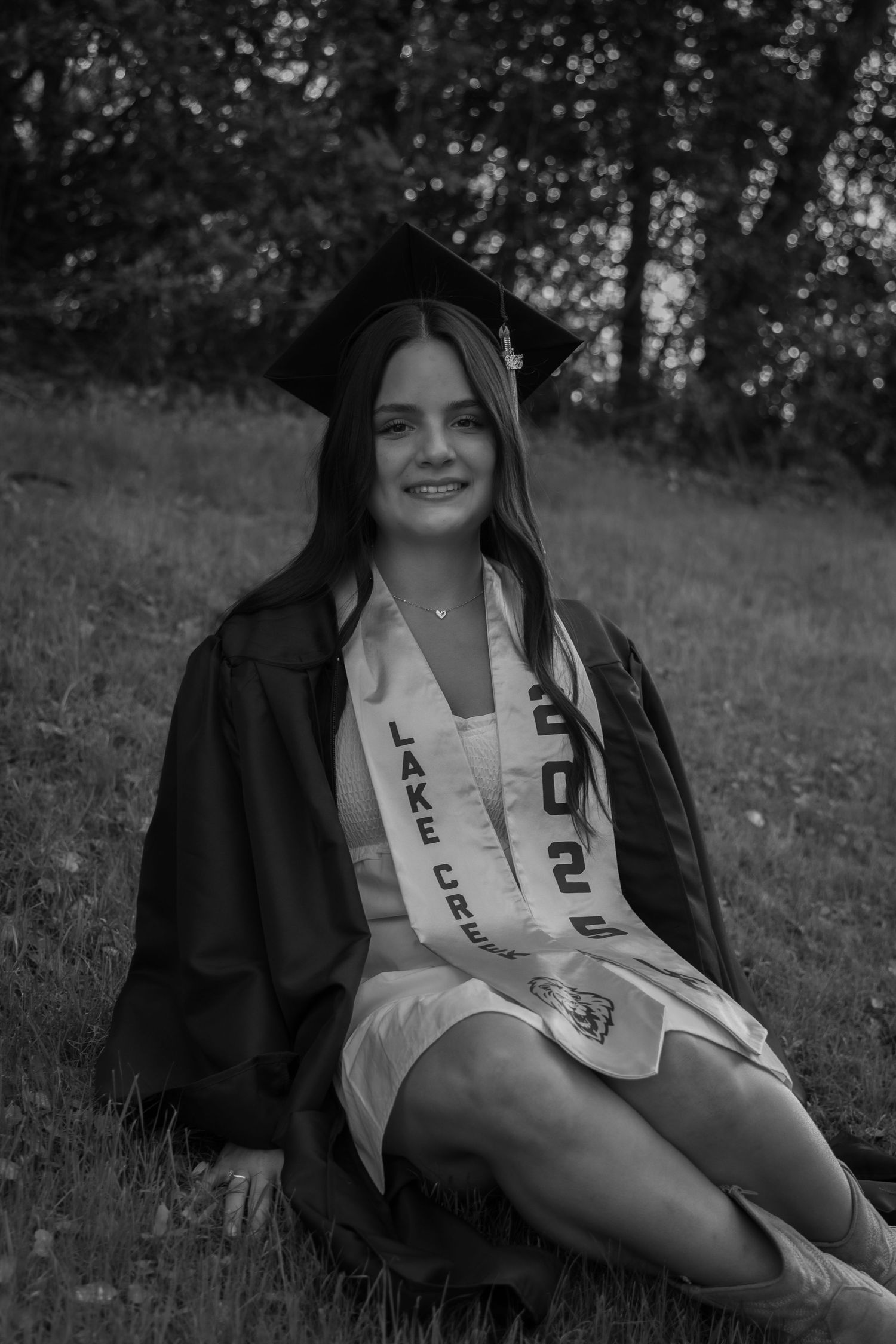 A series of outdoor graduation portraits showing someone in a black cap and gown with white stole laying on grass in a natural setting.