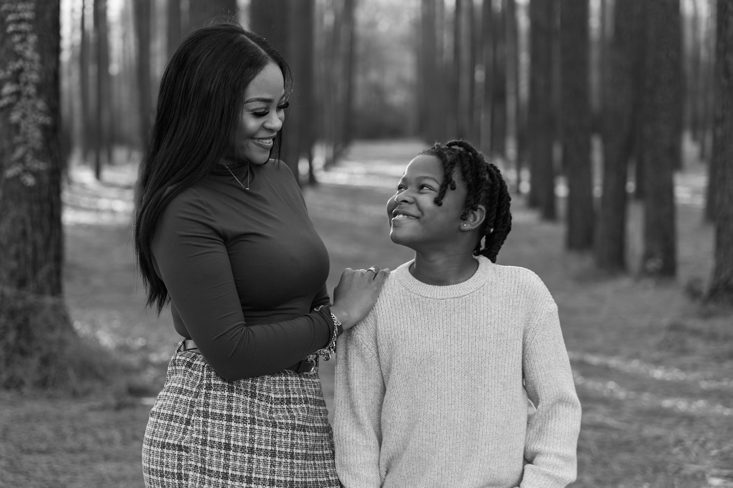 Black and white photo of a woman and young boy smiling at each other in a tree-lined park path.