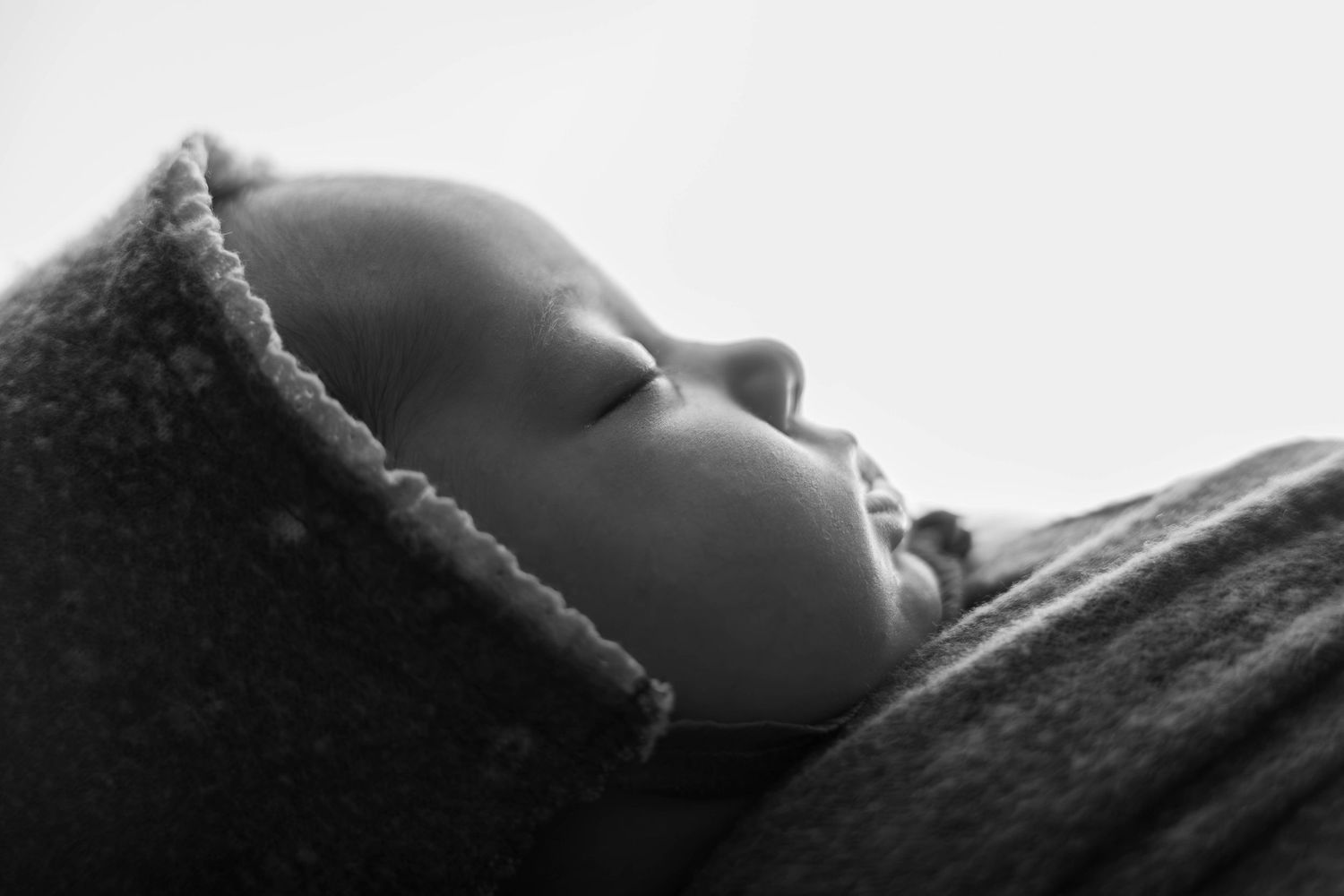 Black and white close-up portrait of a sleeping newborn baby wearing a soft knit hat.