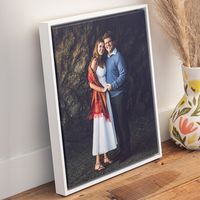 Framed portrait photo print of a couple embracing, displayed on a wooden floor against a white wall.