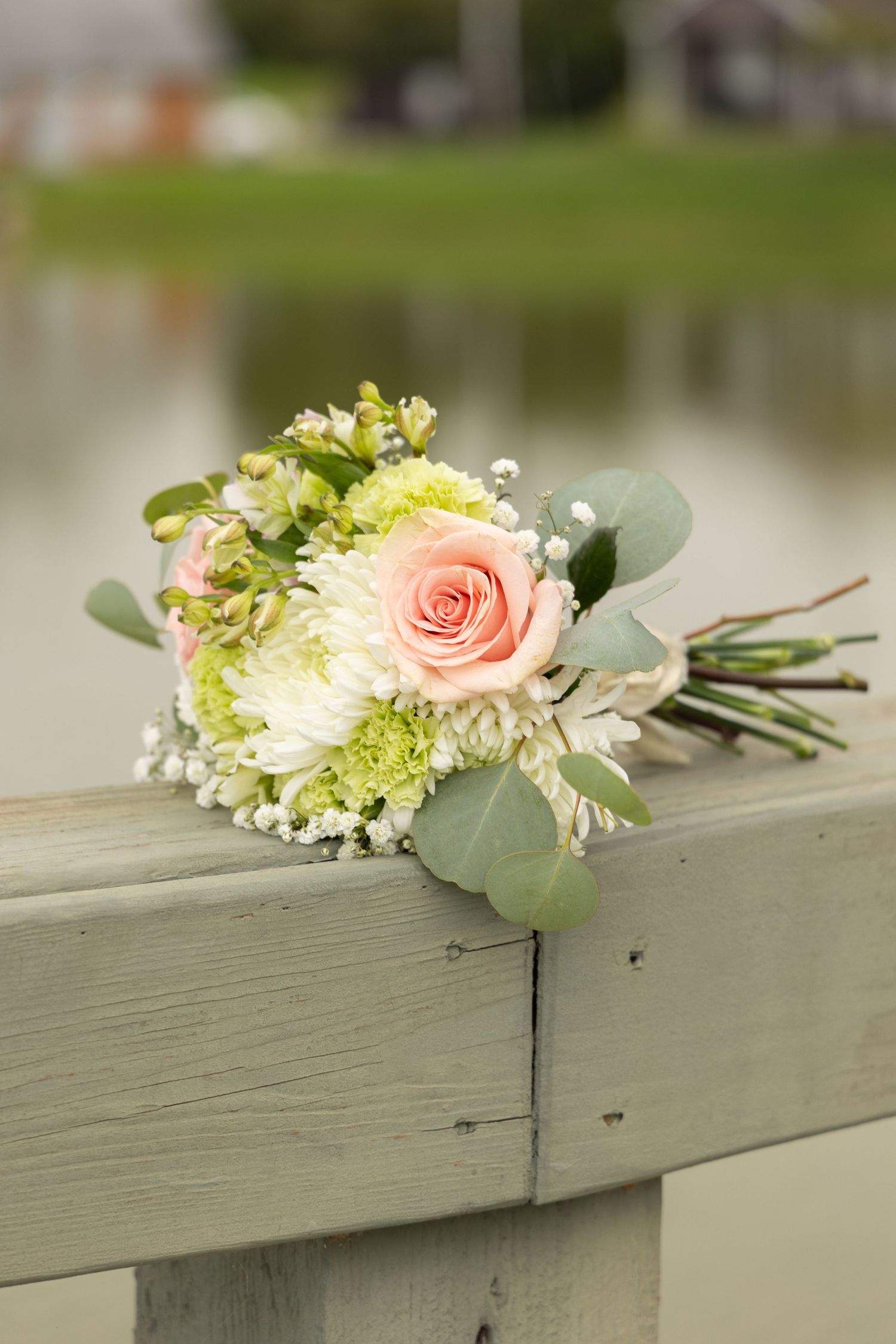 Elegant bridal bouquet with pink roses, white chrysanthemums, and eucalyptus on a wooden railing.
