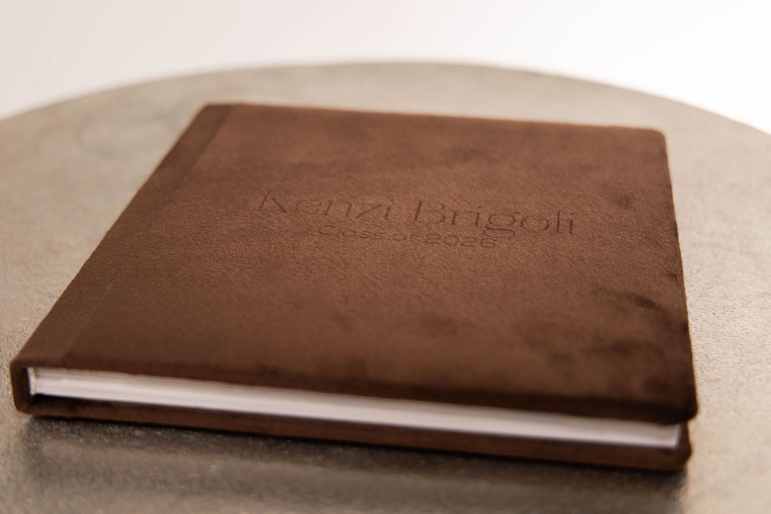 Brown leather hardcover photo book with embossed text resting on a gray surface.