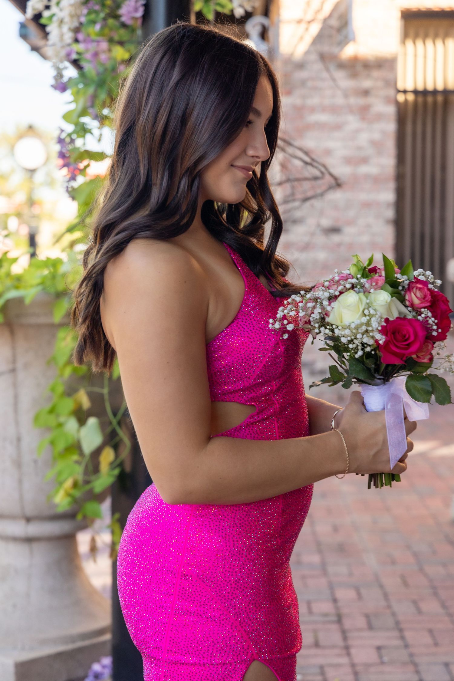 Young woman in a sparkly hot pink formal gown holding a bouquet of red and white roses outdoors.