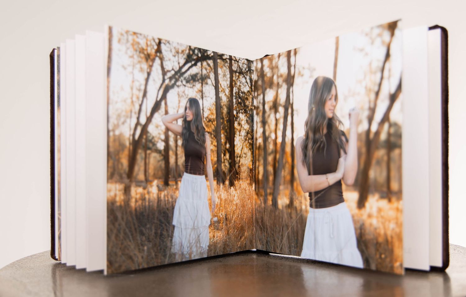 Open photo book displaying a young woman in a white skirt among golden autumn grasses in a warm outdoor setting.