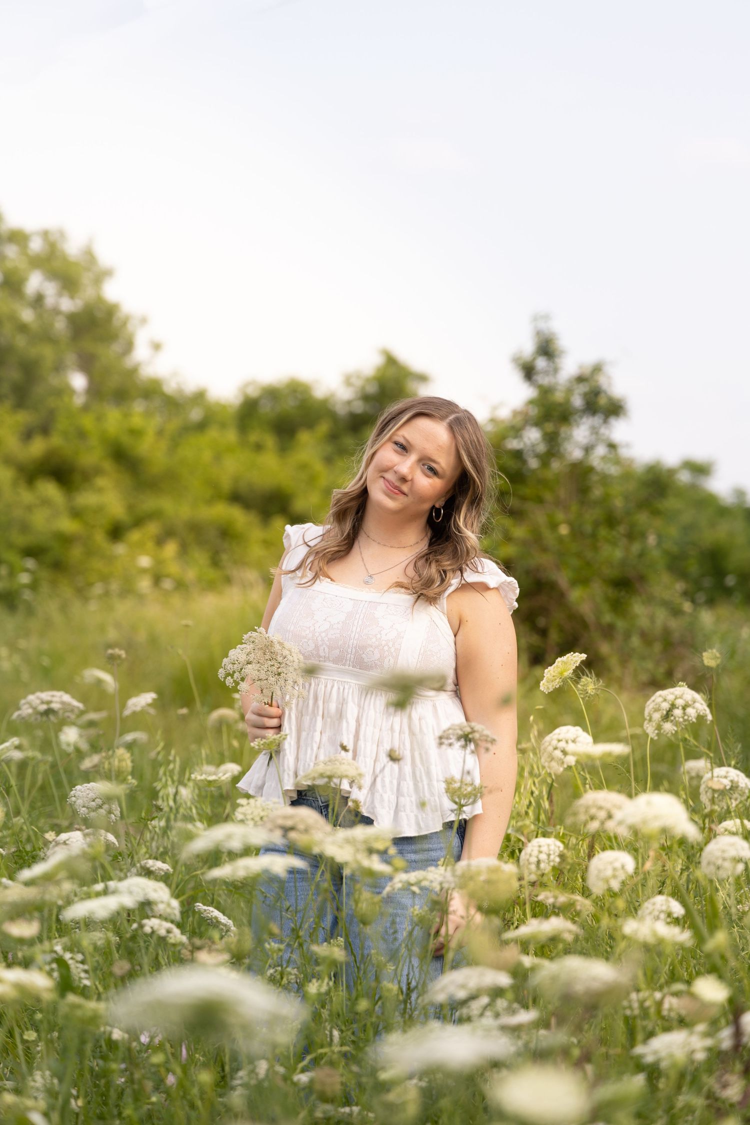 A person sits joyfully among blooming Queen Anne's Lace wildflowers on a bright summer day.