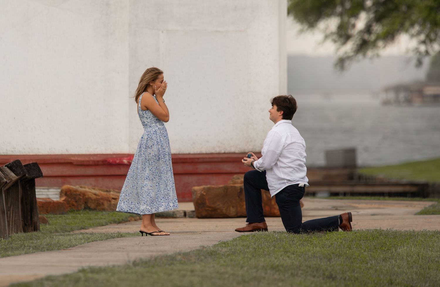 Man proposes on one knee to surprised woman outdoors near historic building at dusk.