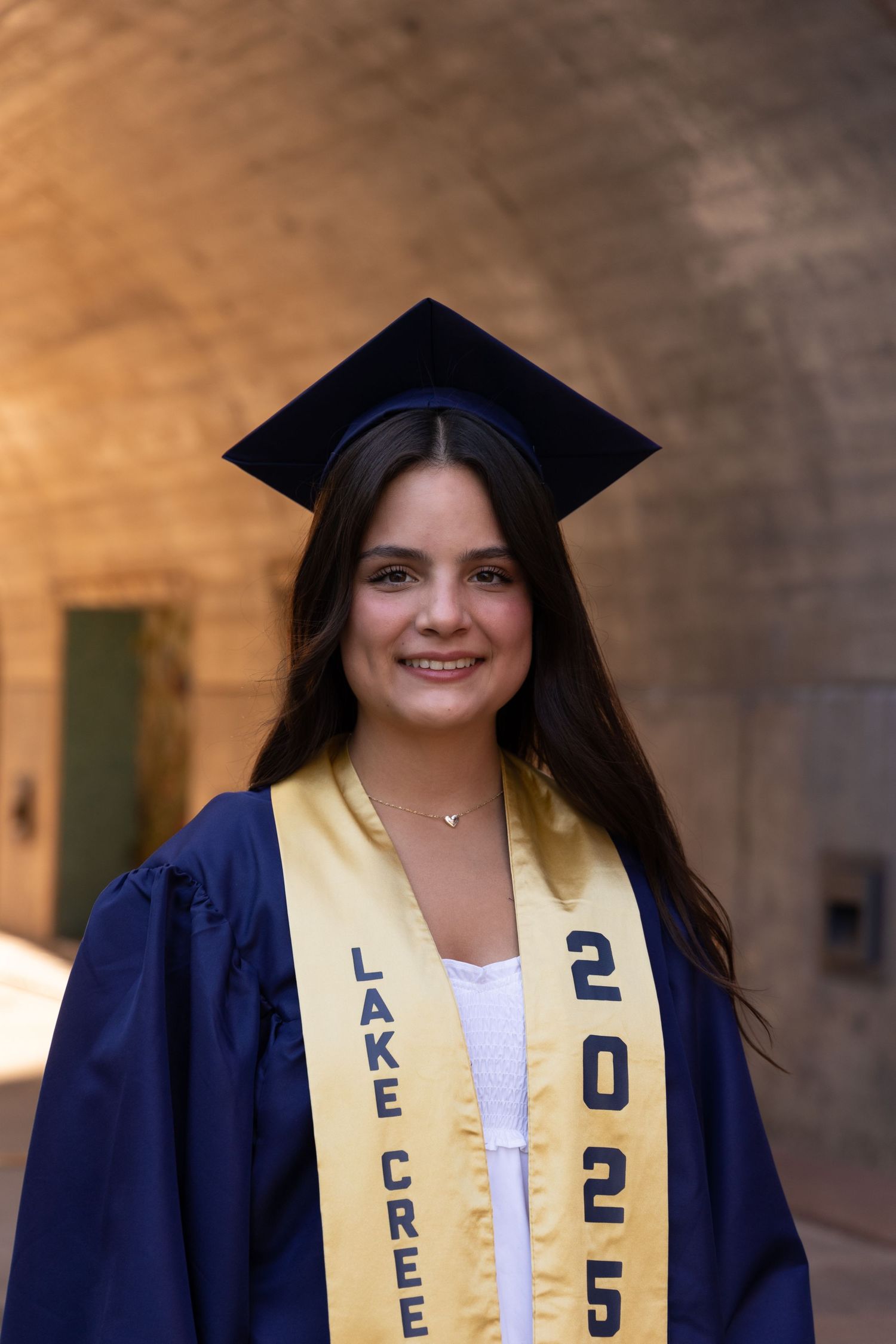 Smiling female graduate in navy cap and gown wearing a gold Lake Creek 2025 graduation stole.