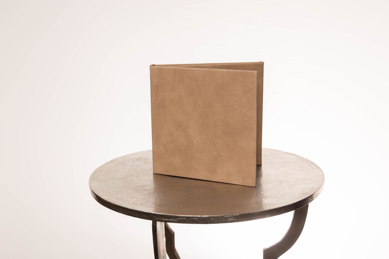 A tan leather square binder standing upright on a round metal side table against a white background.