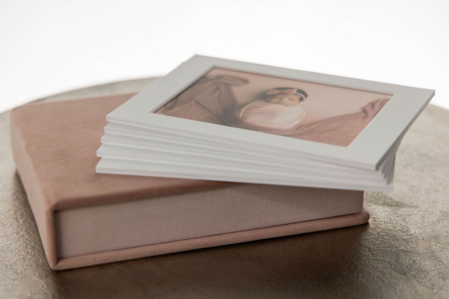 Elegant wedding photo album with pink velvet box and framed bridal portrait on textured surface.