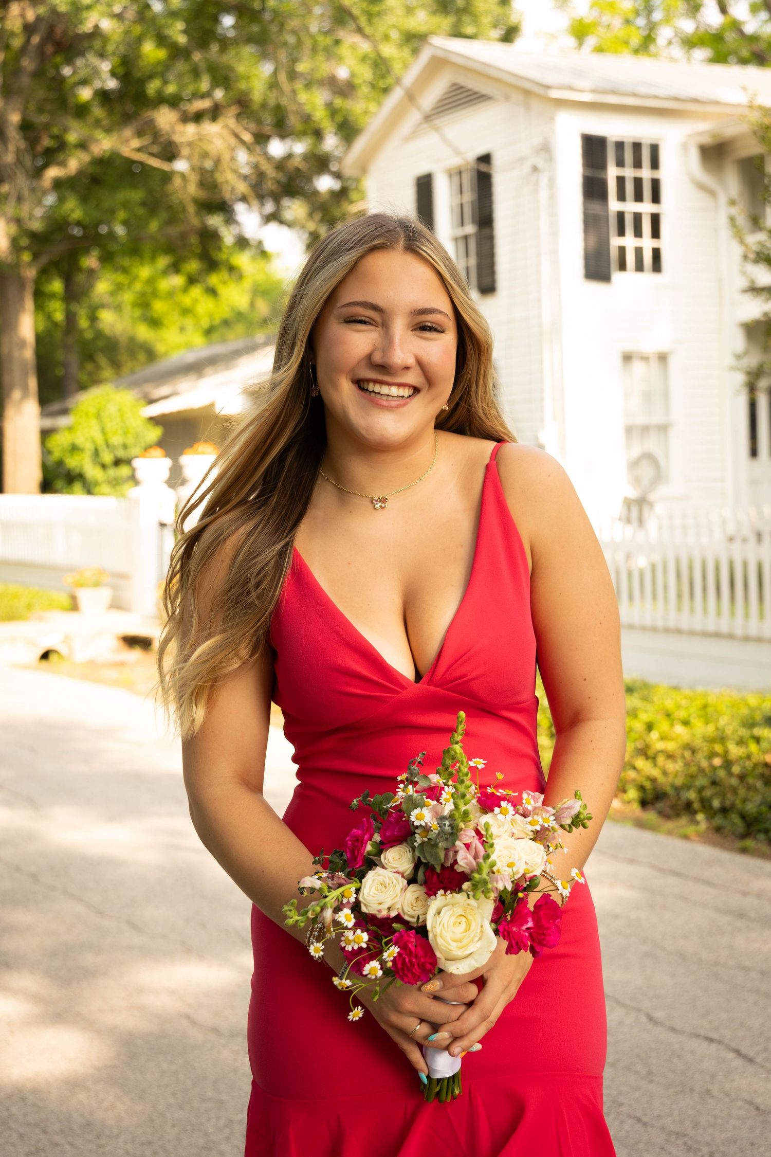 Smiling young woman in a red dress holding a bouquet of flowers outdoors.
