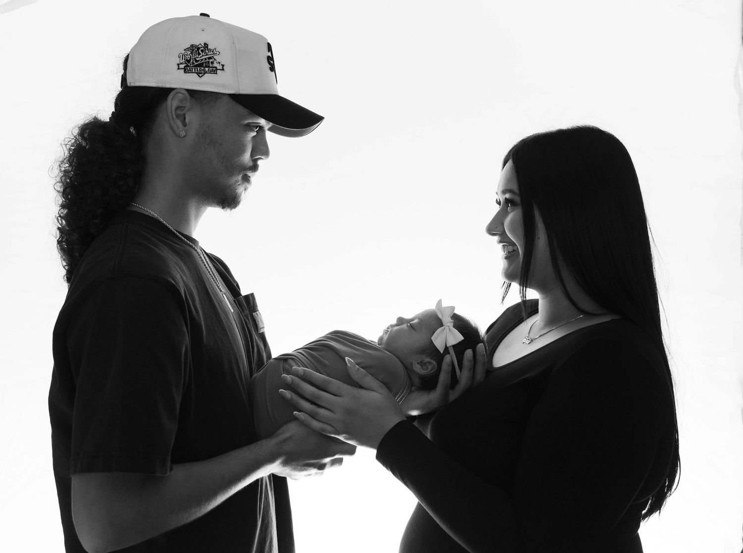Black and white photo of a couple tenderly holding a newborn baby together in a bright studio setting.